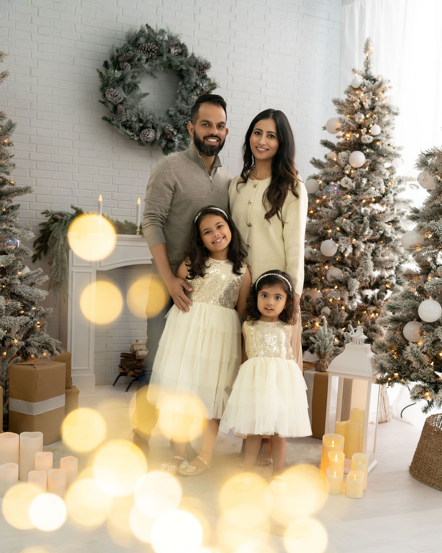 Festive family photo with bokeh lights and Christmas decorations in a bright white studio setting.