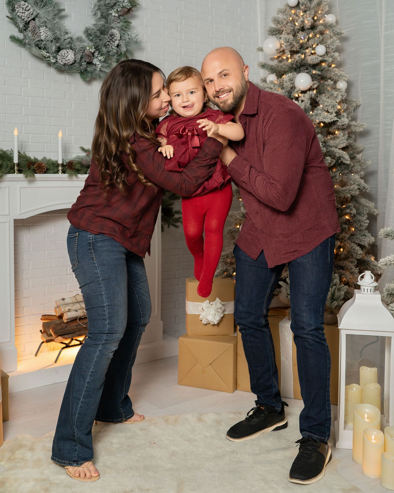 Playful family interaction captured in burgundy outfits against Christmas decorated studio setting.