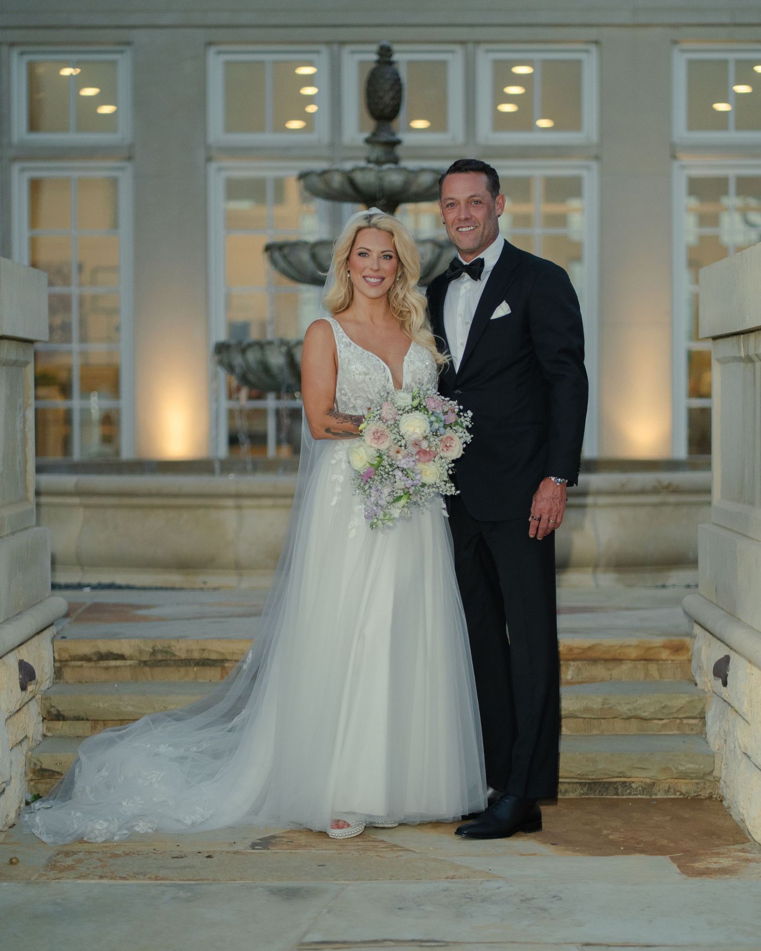 Wedding couple portraits on illuminated porch steps of a grand white building at dusk.