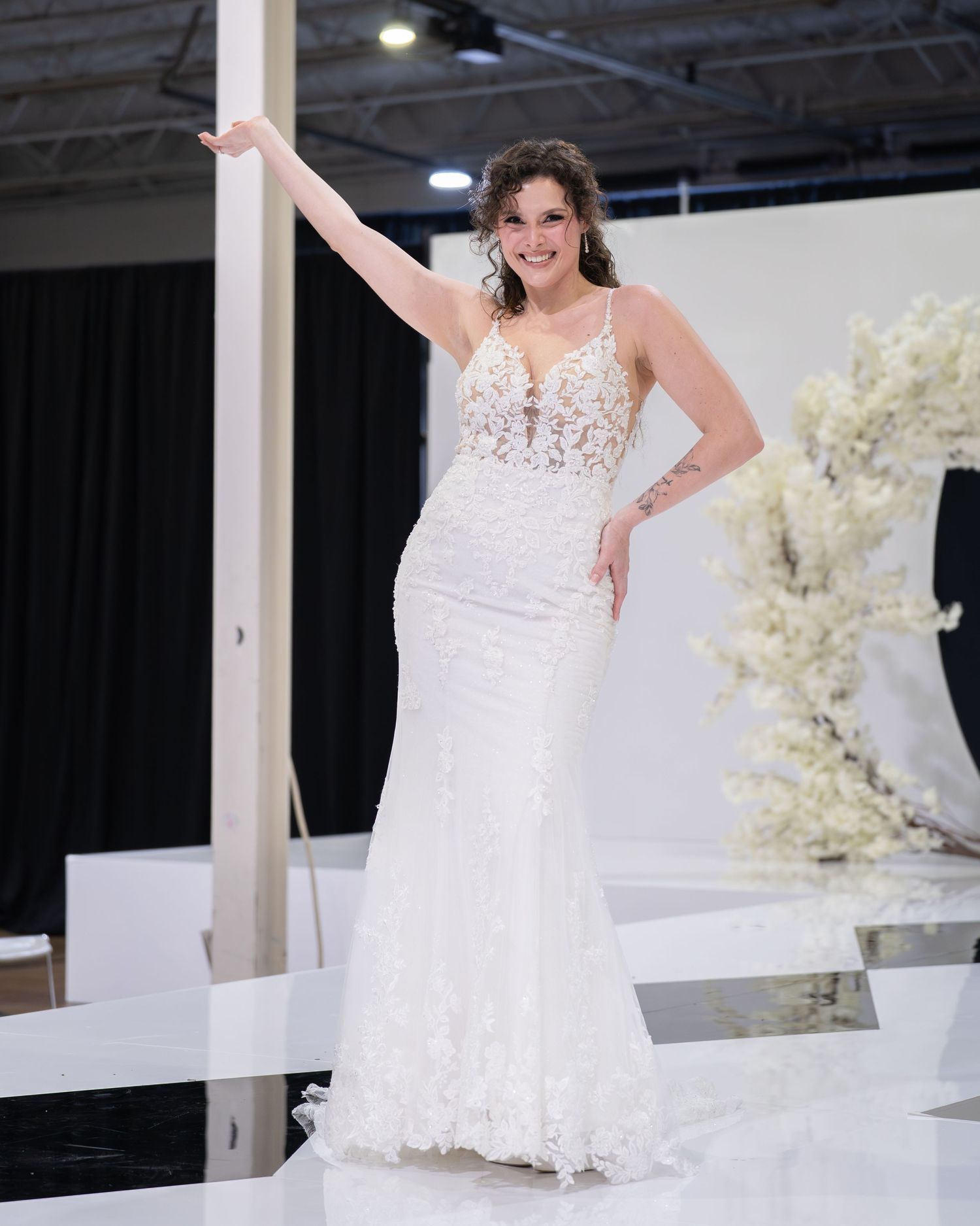 Plus-size model wearing a white lace mermaid wedding gown with plunging neckline on a bridal runway.