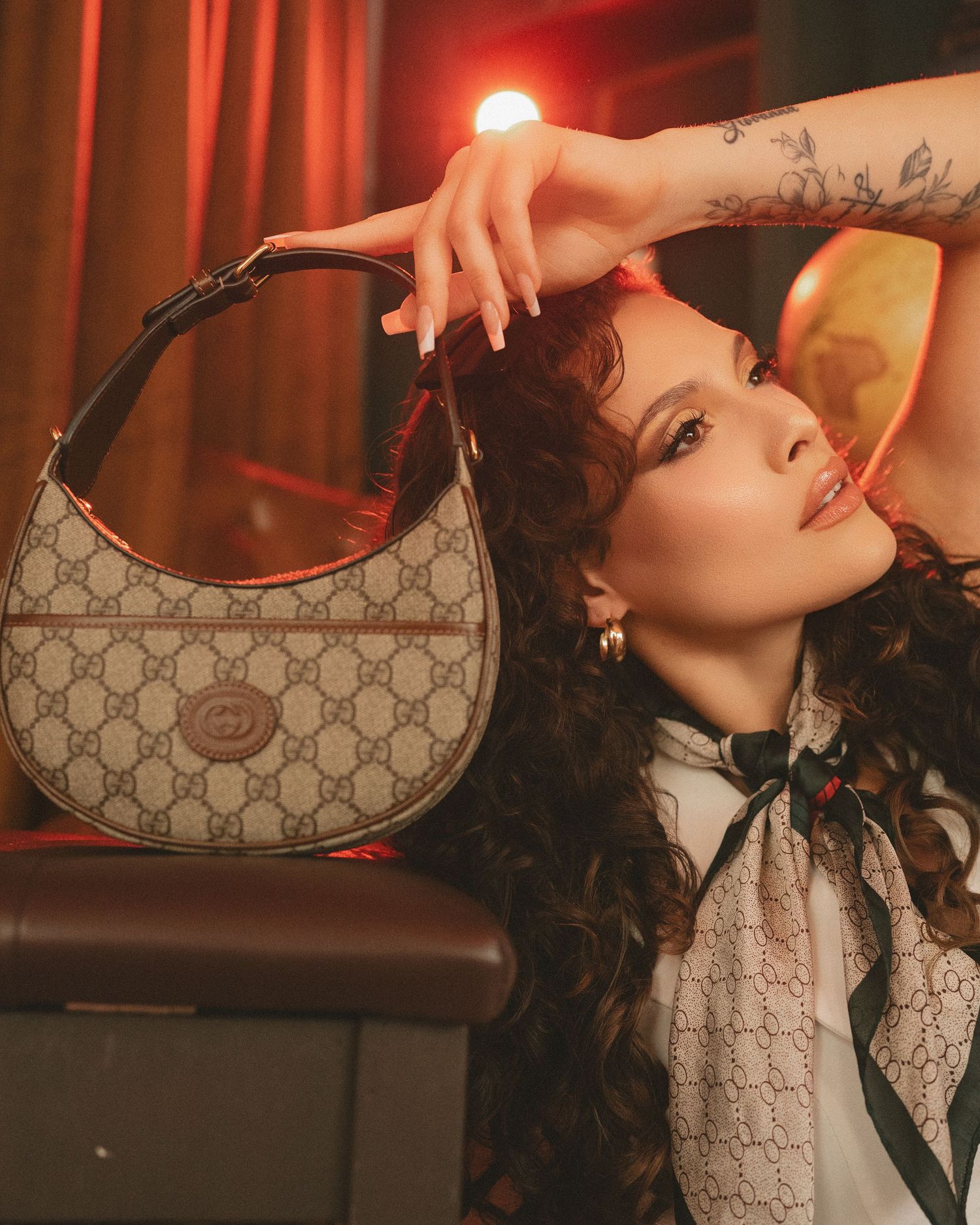 Woman posing with a Gucci GG Supreme monogram hobo bag in a warmly lit setting.