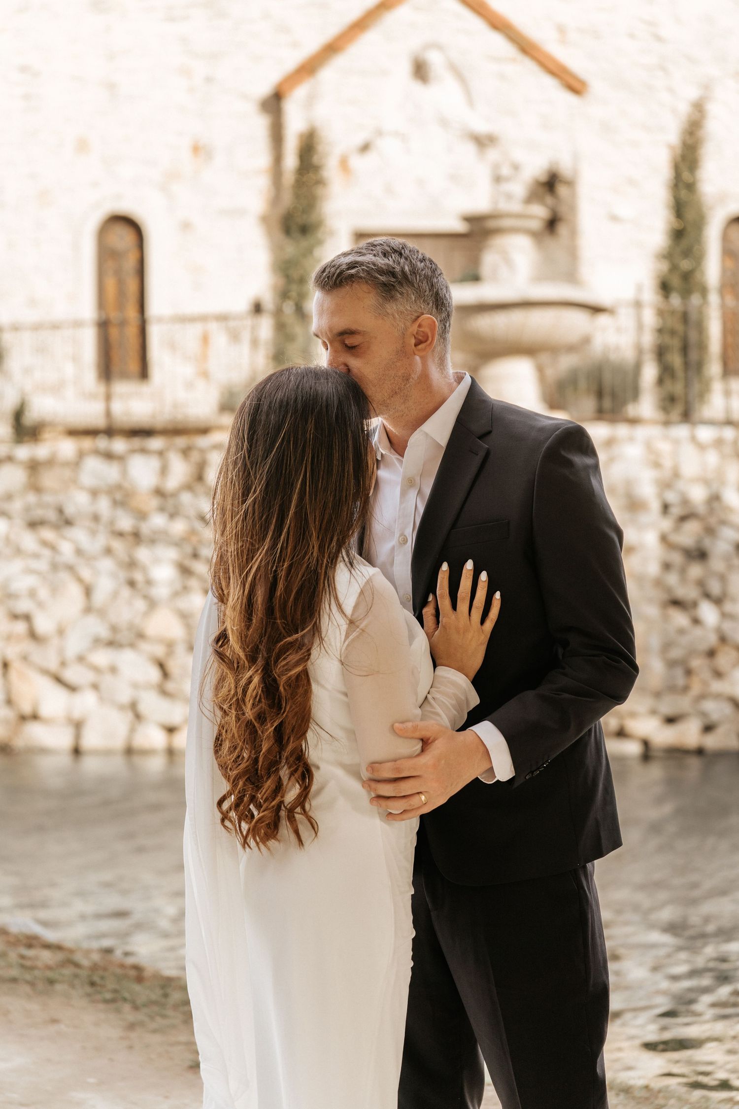 Romantic couple in formal attire sharing intimate moments against a stone wall backdrop.