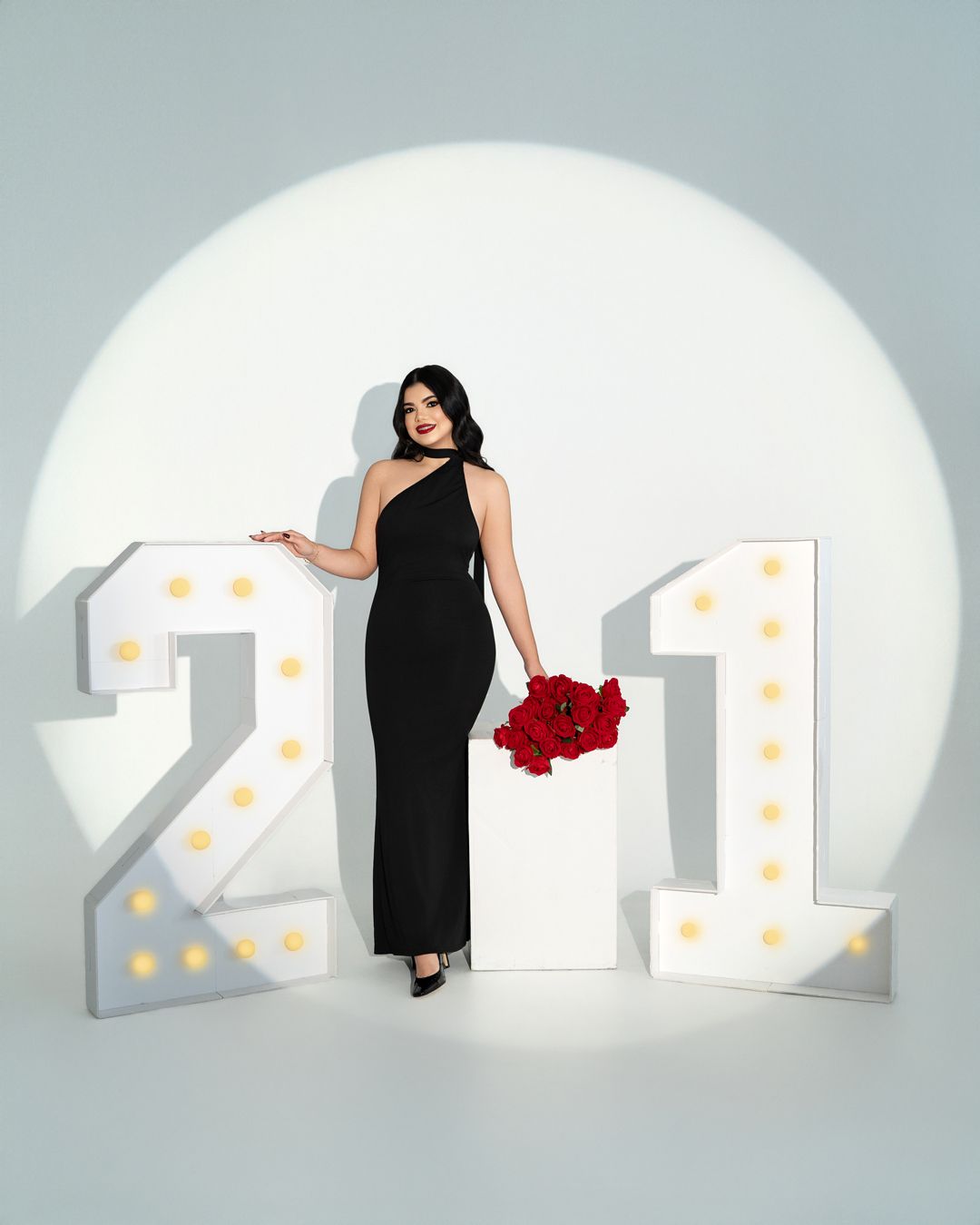 Studio portrait with illuminated number backdrop and figure holding red roses.