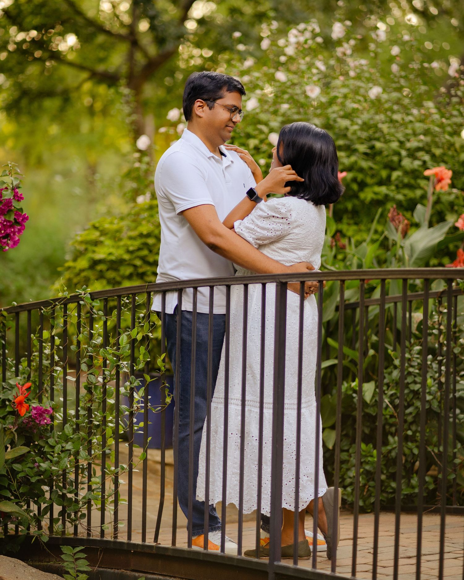 Couple sharing a romantic moment on a garden bridge surrounded by lush greenery.