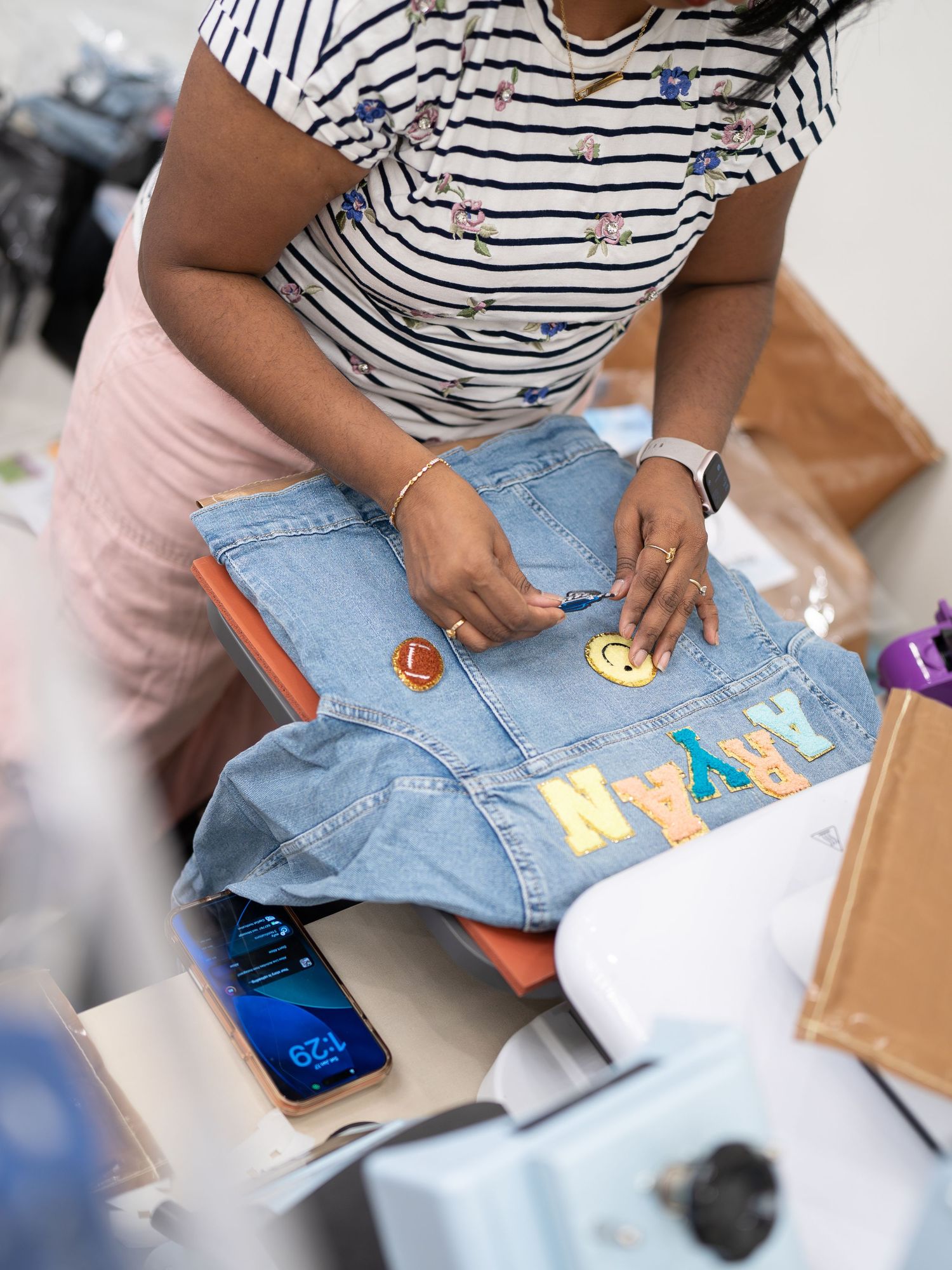 Person wearing striped shirt applies colorful iron-on patches to denim jeans in a creative DIY crafting sequence.