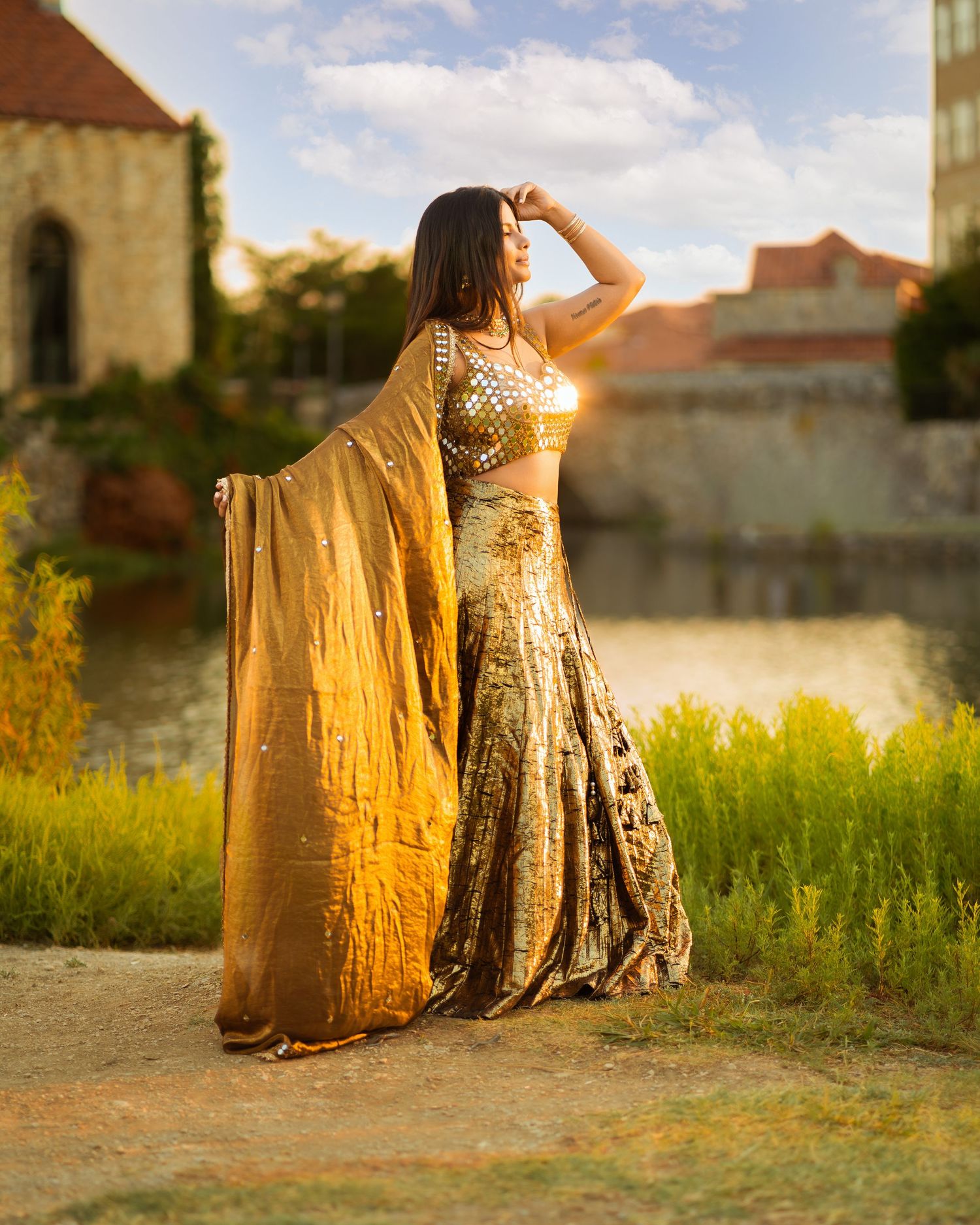 Two people sitting on ground at sunset near old stone building with golden sunlight.