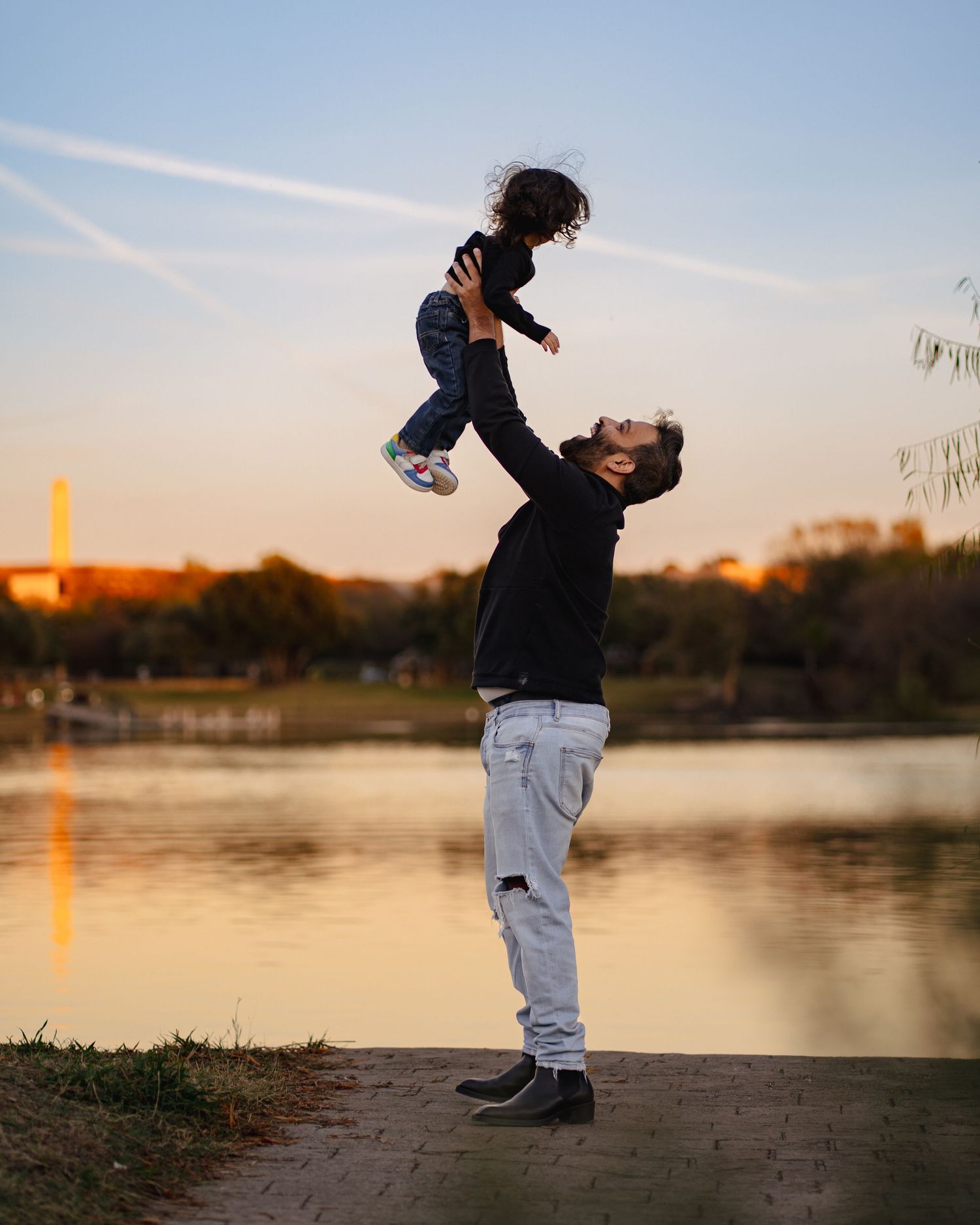 Silhouettes play together at sunset by a tranquil lake with golden light reflecting off the water's surface.