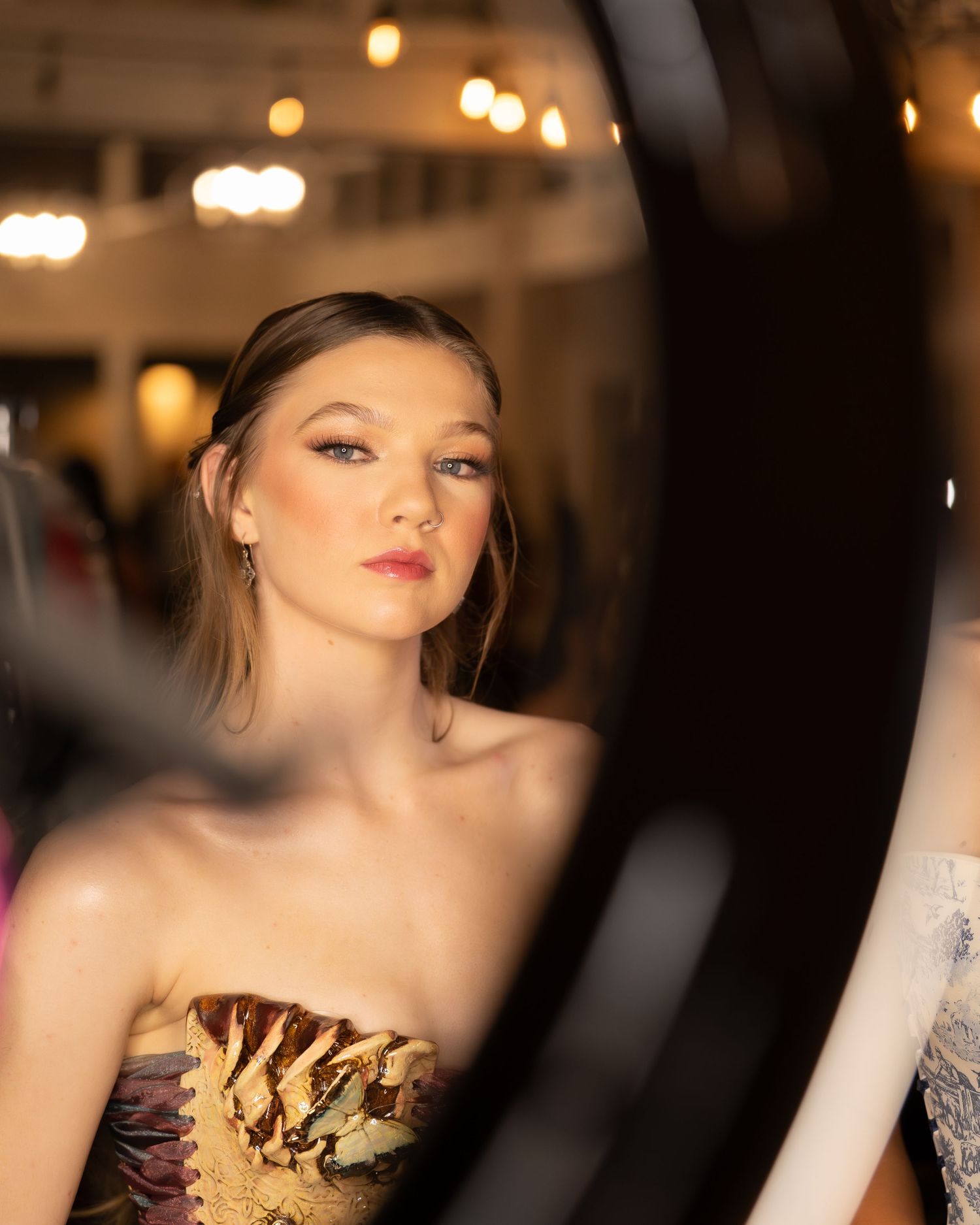 A glamorous fashion model poses in a strapless gold dress under warm lighting at an evening event.