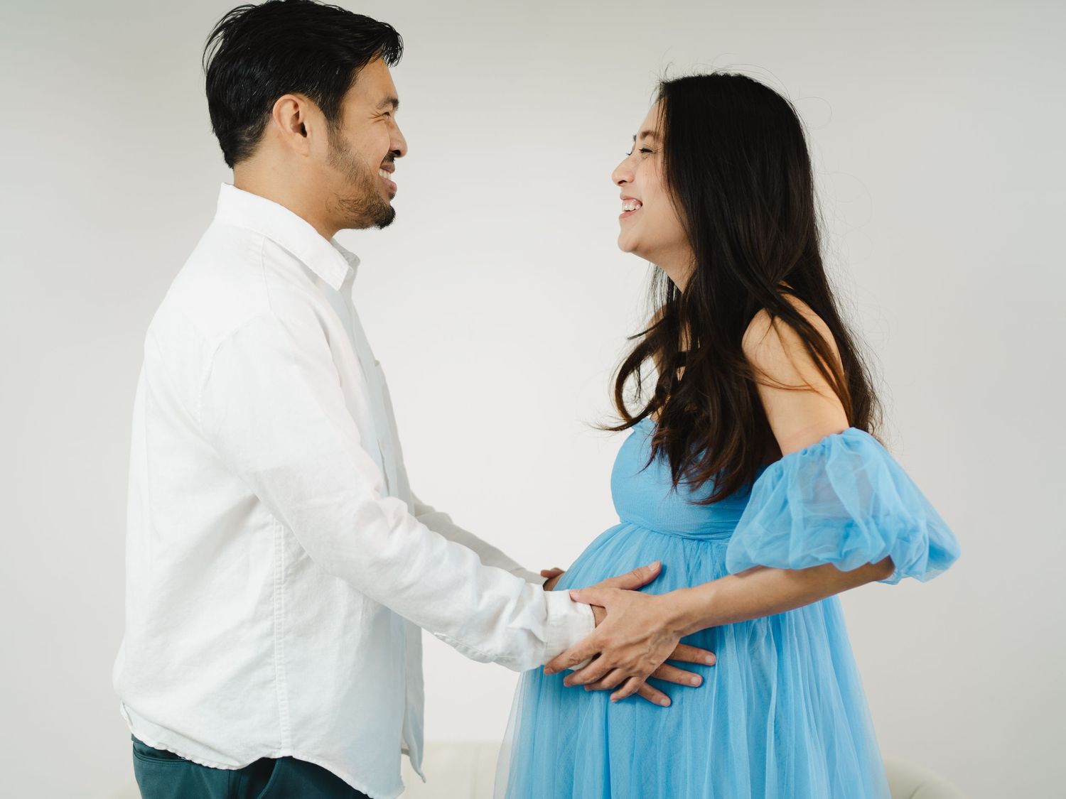 A couple sharing a joyful moment, the woman in a blue tulle maternity dress holding hands with a man in a white shirt.