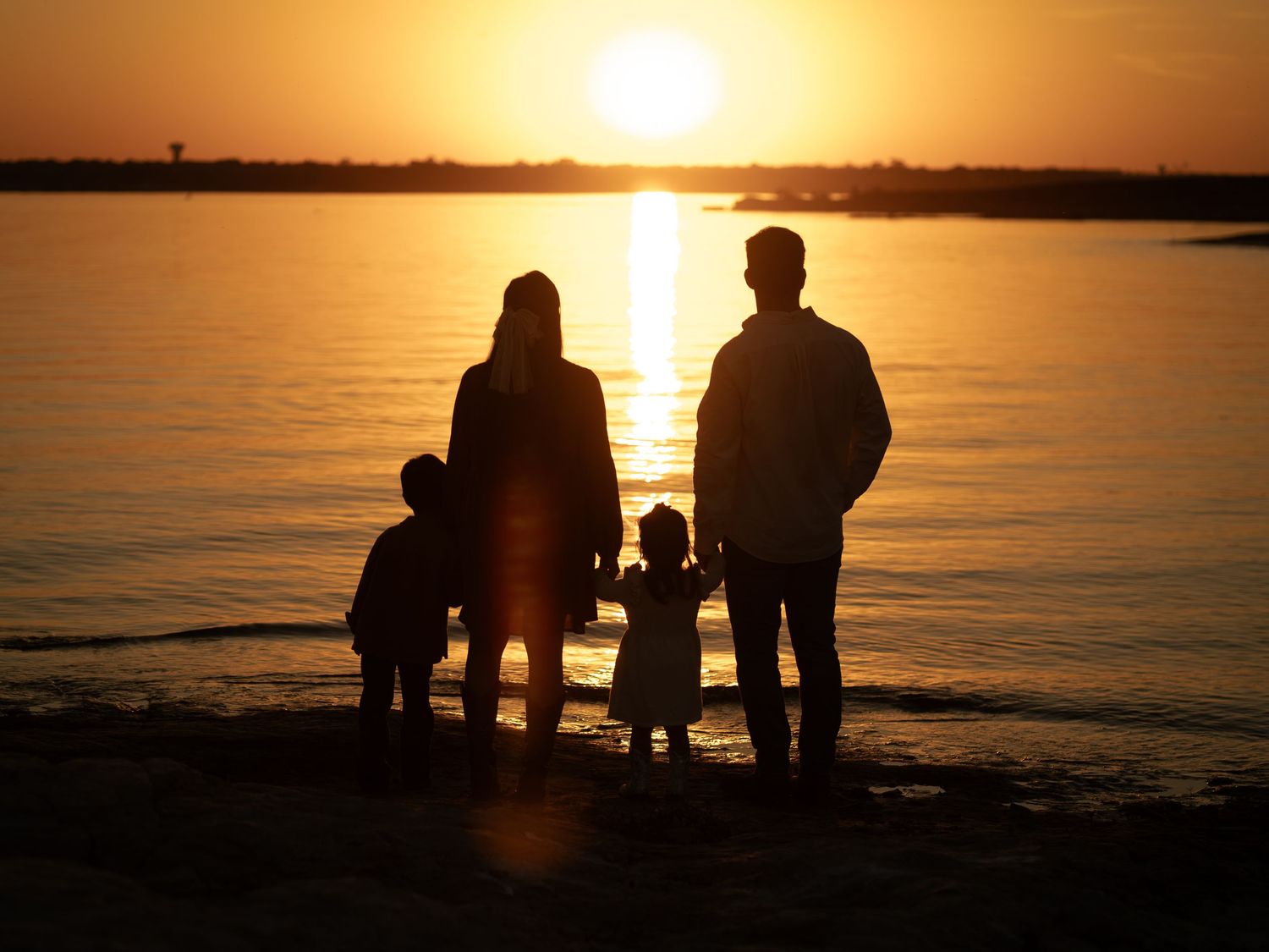 Silhouettes of people gathered at the beach during a golden sunset over calm waters.