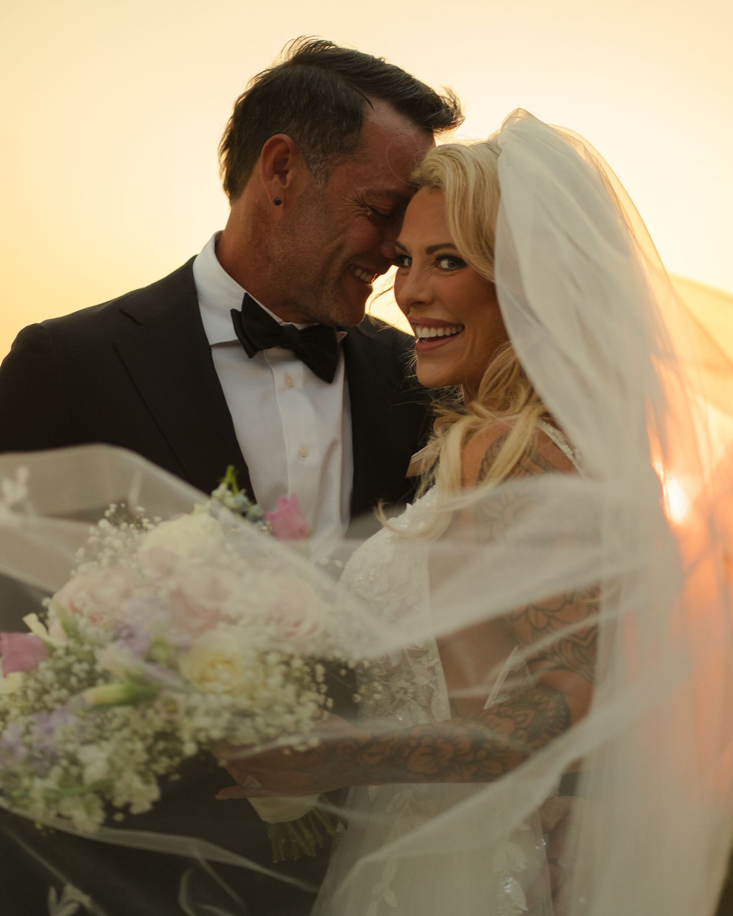 Intimate wedding couple portraits at golden hour with flowing veil and white floral bouquet.