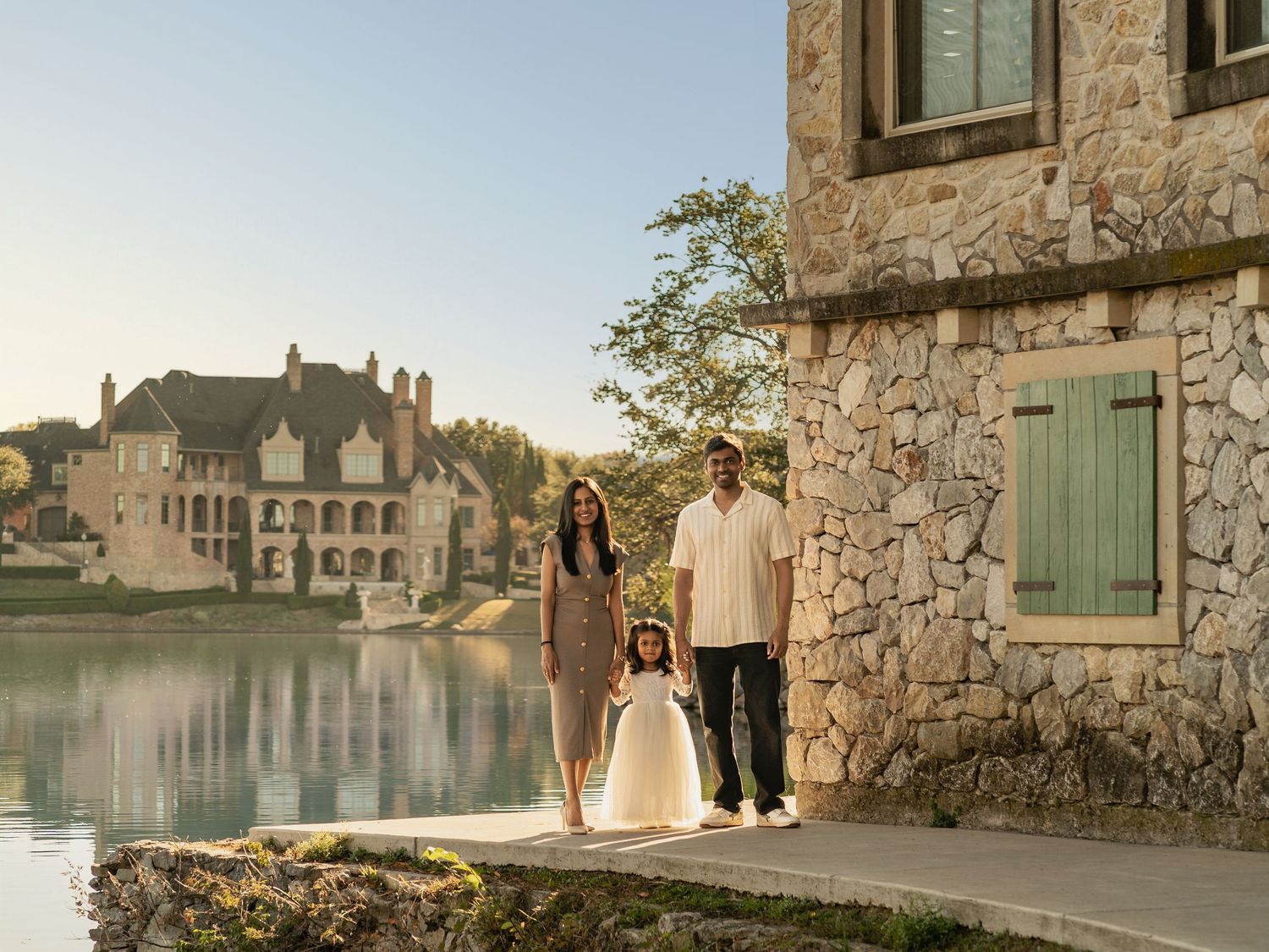 Family walking along stone building exterior beside a scenic waterfront at sunset.