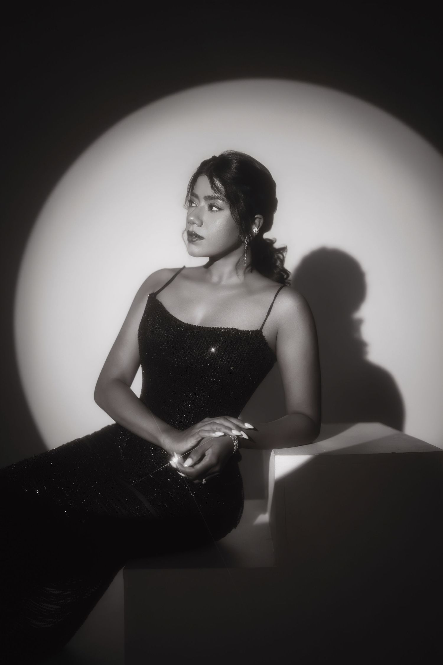 Black and white portrait of a young woman in a sequined dress, posed elegantly under a circular spotlight.