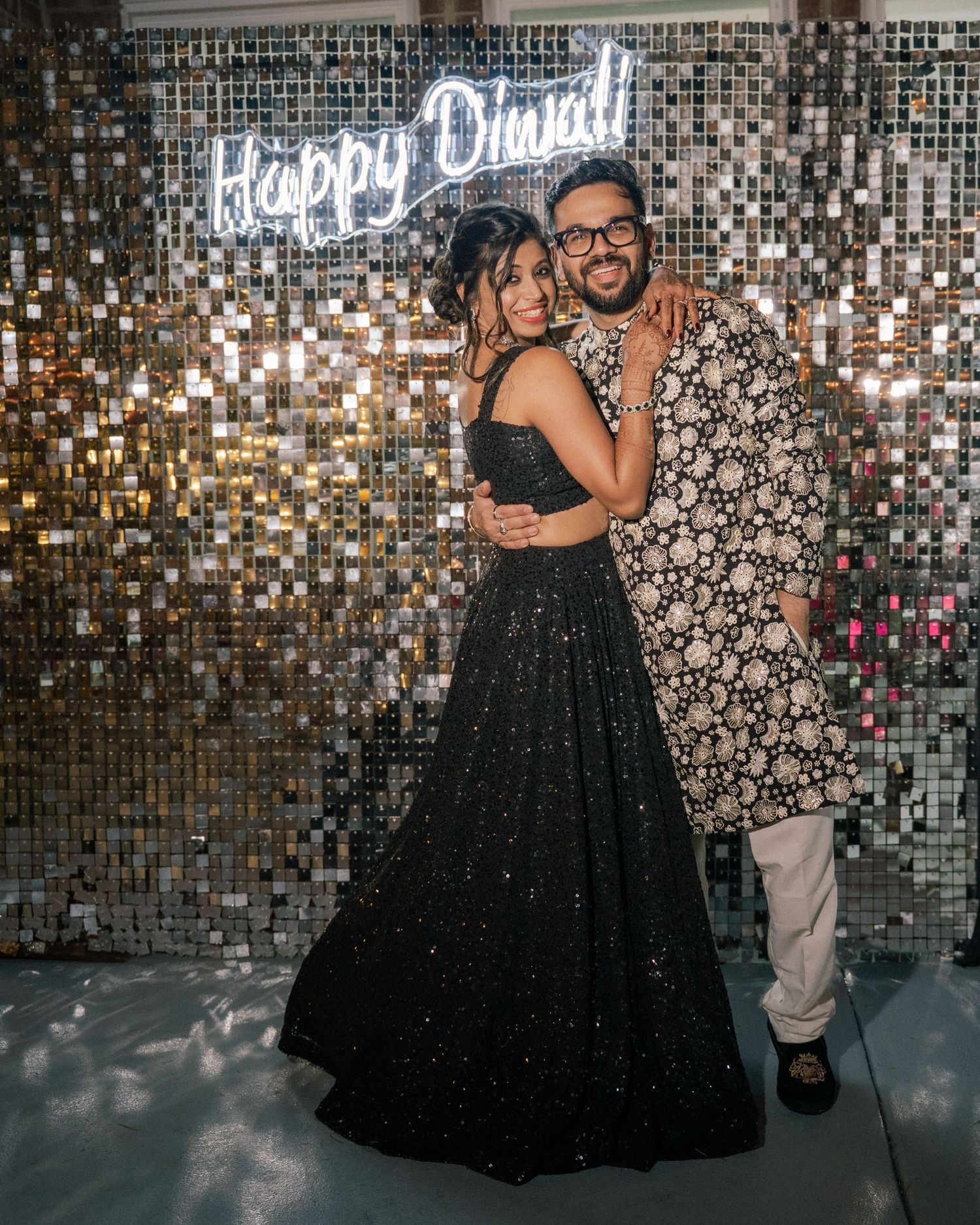A couple poses in front of a shimmering silver sequin wall at what appears to be a celebration or event.