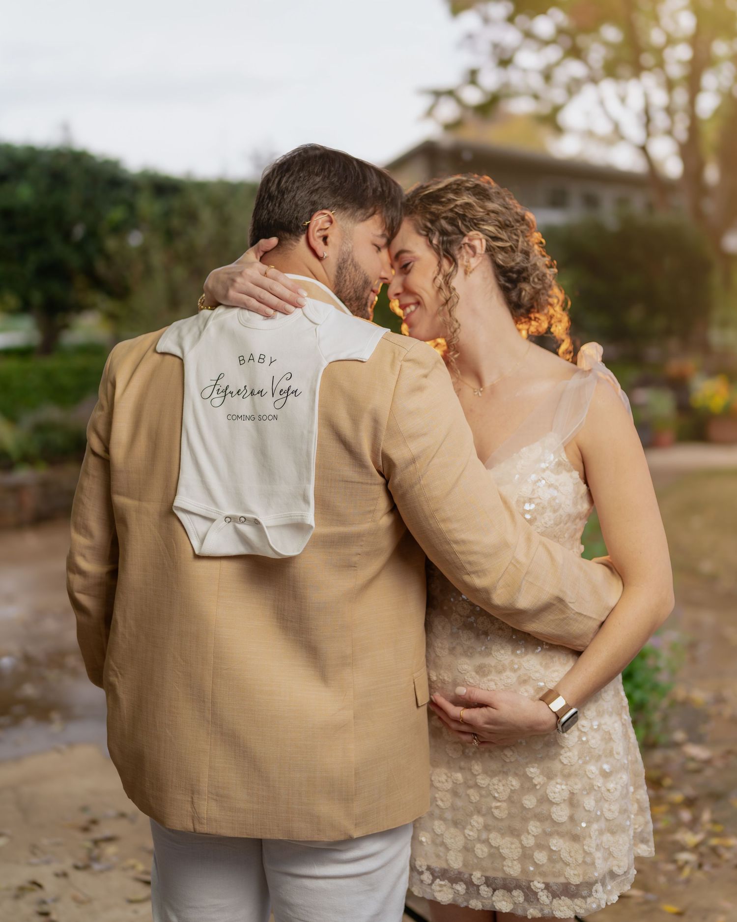 Romantic couple in beige attire embracing outdoors while holding special announcement.