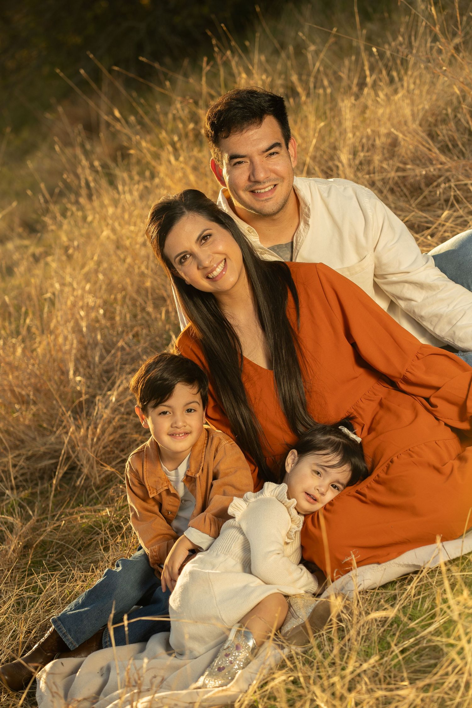 Family relaxing together in tall autumn grass during golden hour.