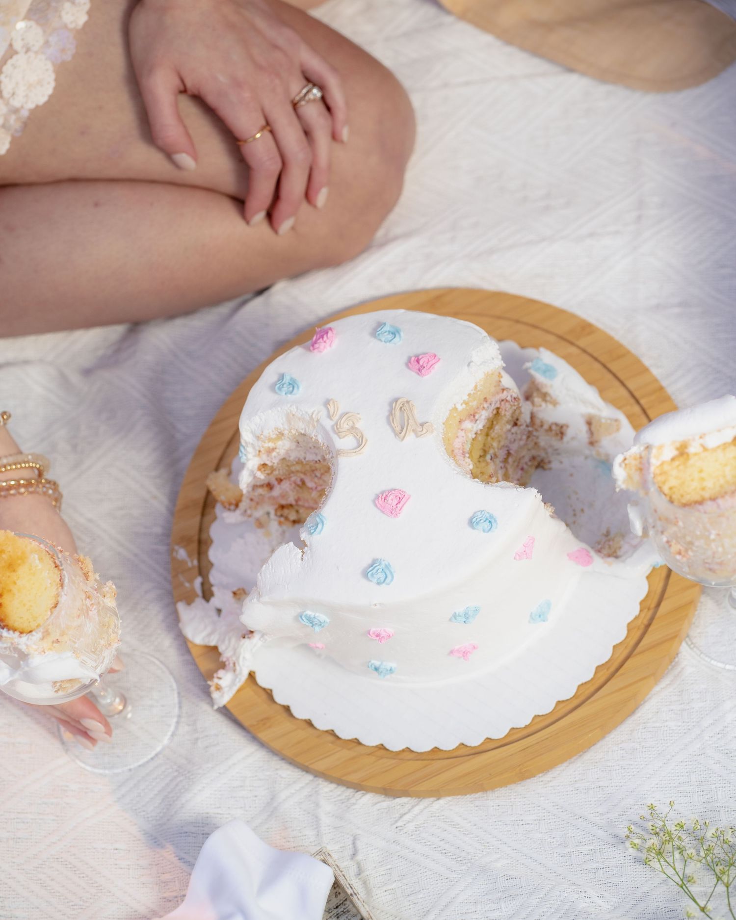 A white frosted cake with pink and blue heart decorations being cut and served on a wooden board.