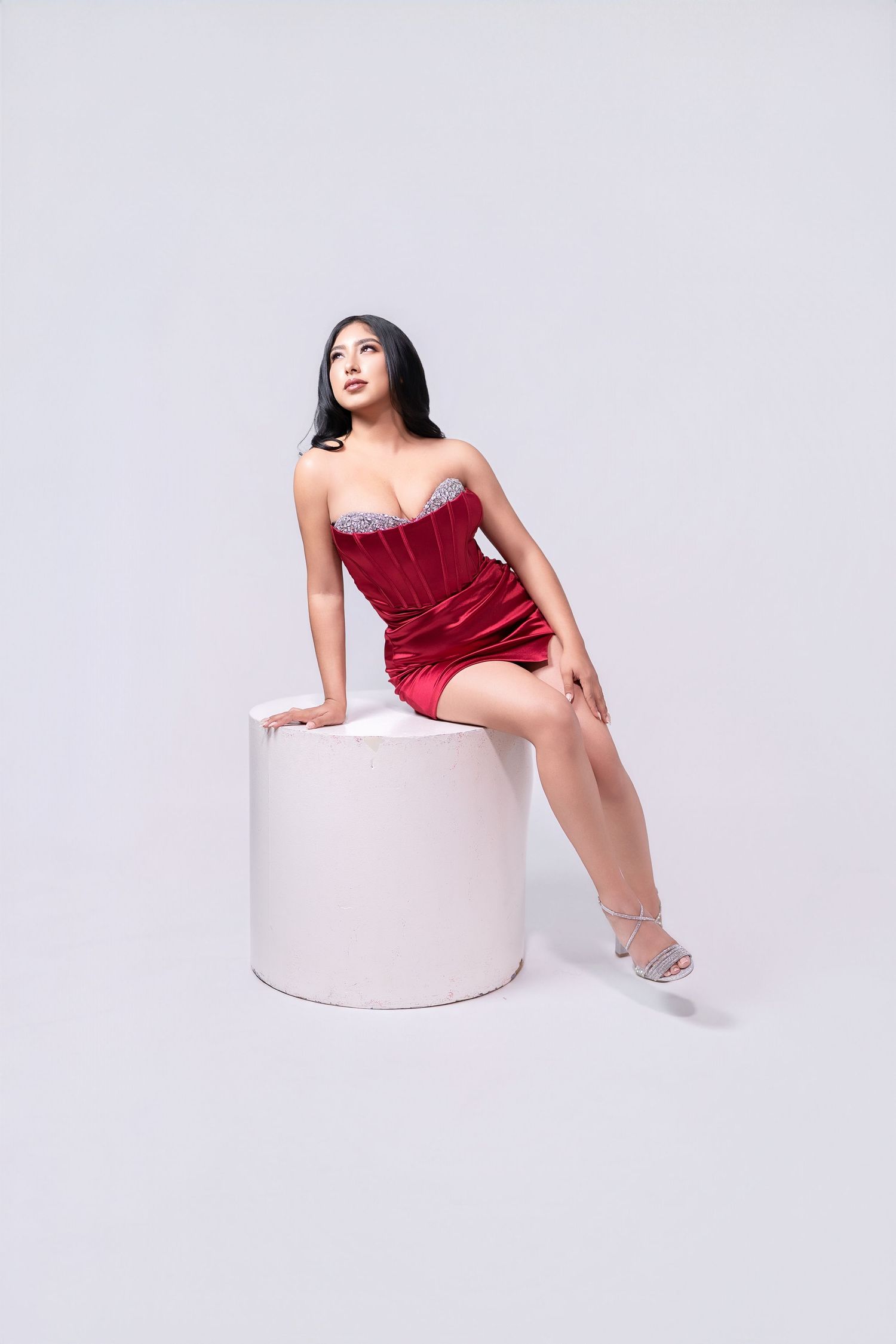 Model in red velvet dress poses elegantly on white cylindrical platform.