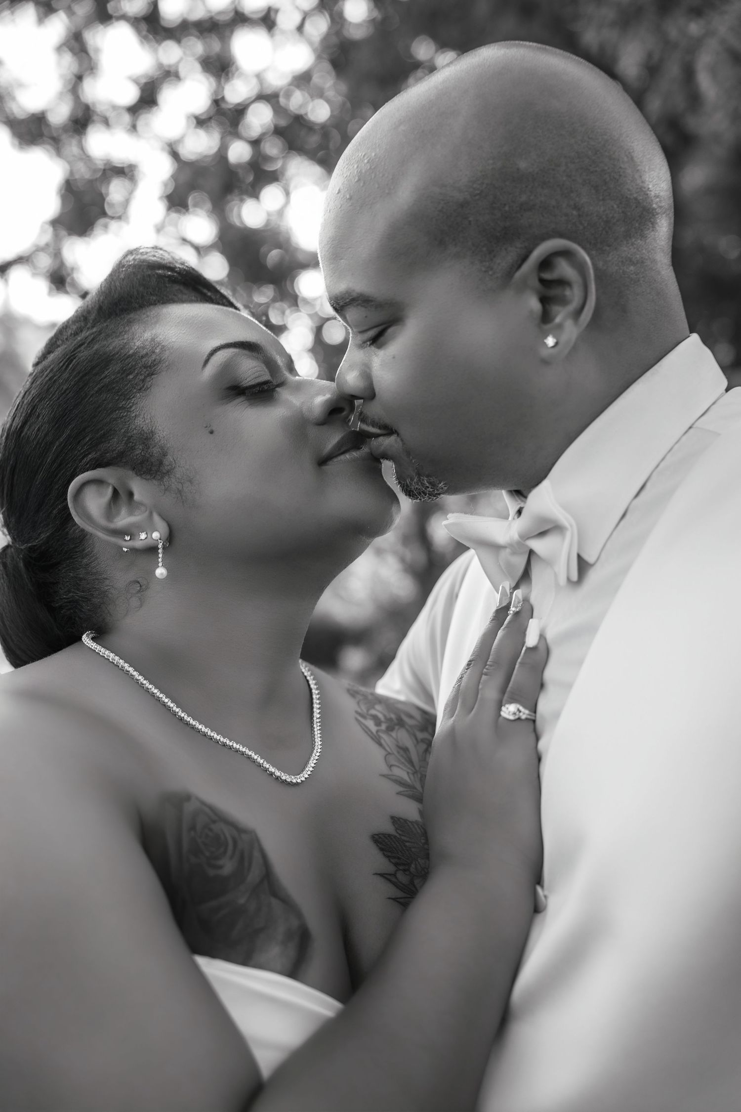 Intimate black and white wedding photo of couple in close embrace, bride in white dress with visible tattoo, groom in white shirt.