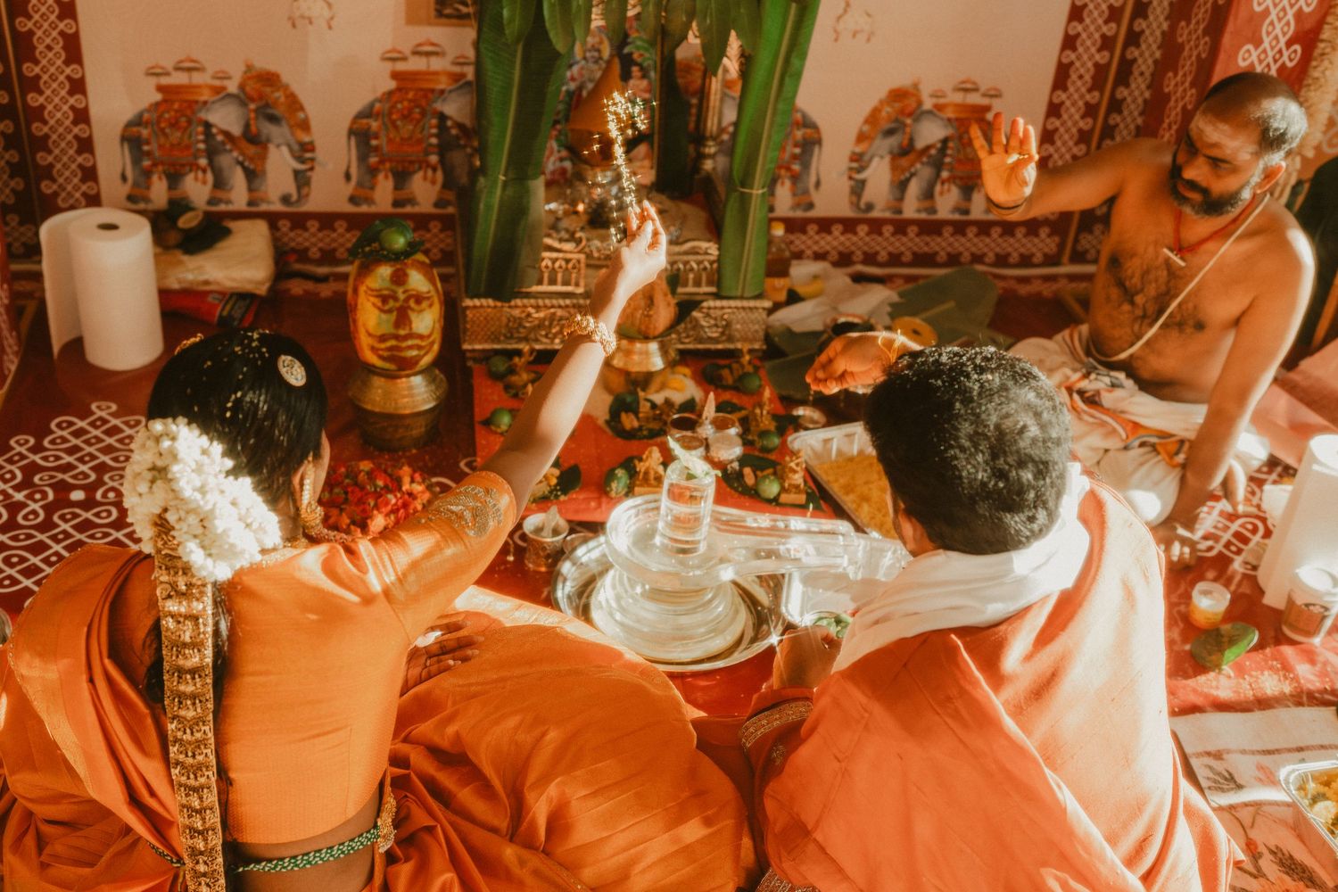 Hindu priests performing a traditional puja ceremony with offerings before a deity shrine, dressed in orange robes.