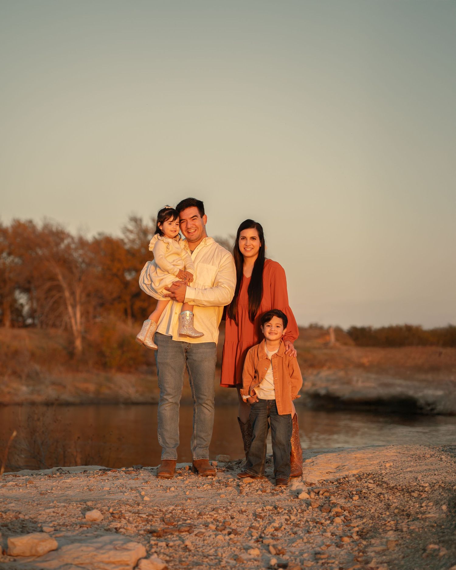Family enjoying sunset together on a rocky beach shore during golden hour.