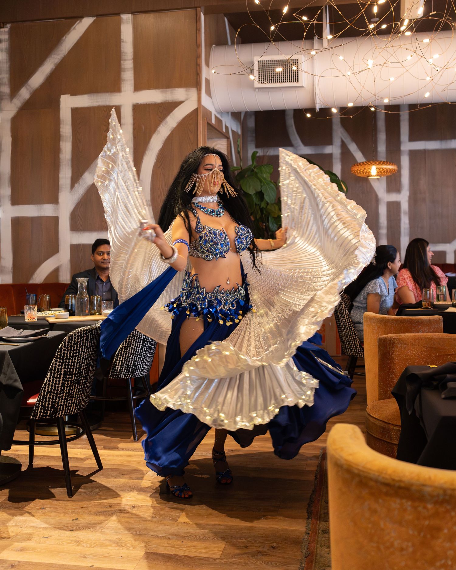 Dancers in flowing white and blue dresses perform on stage during an entertainment show at an indoor venue.