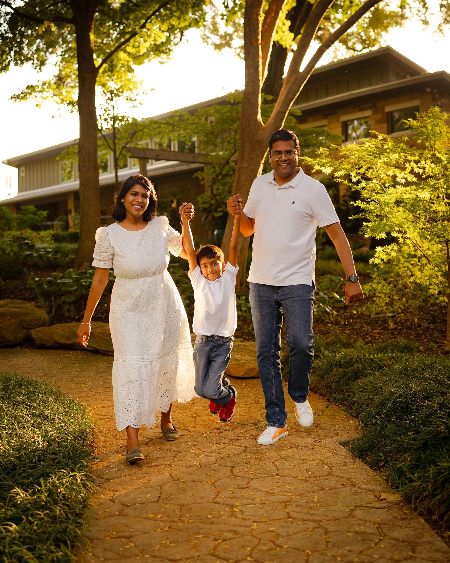 Family walking together on brick path through garden at sunset.