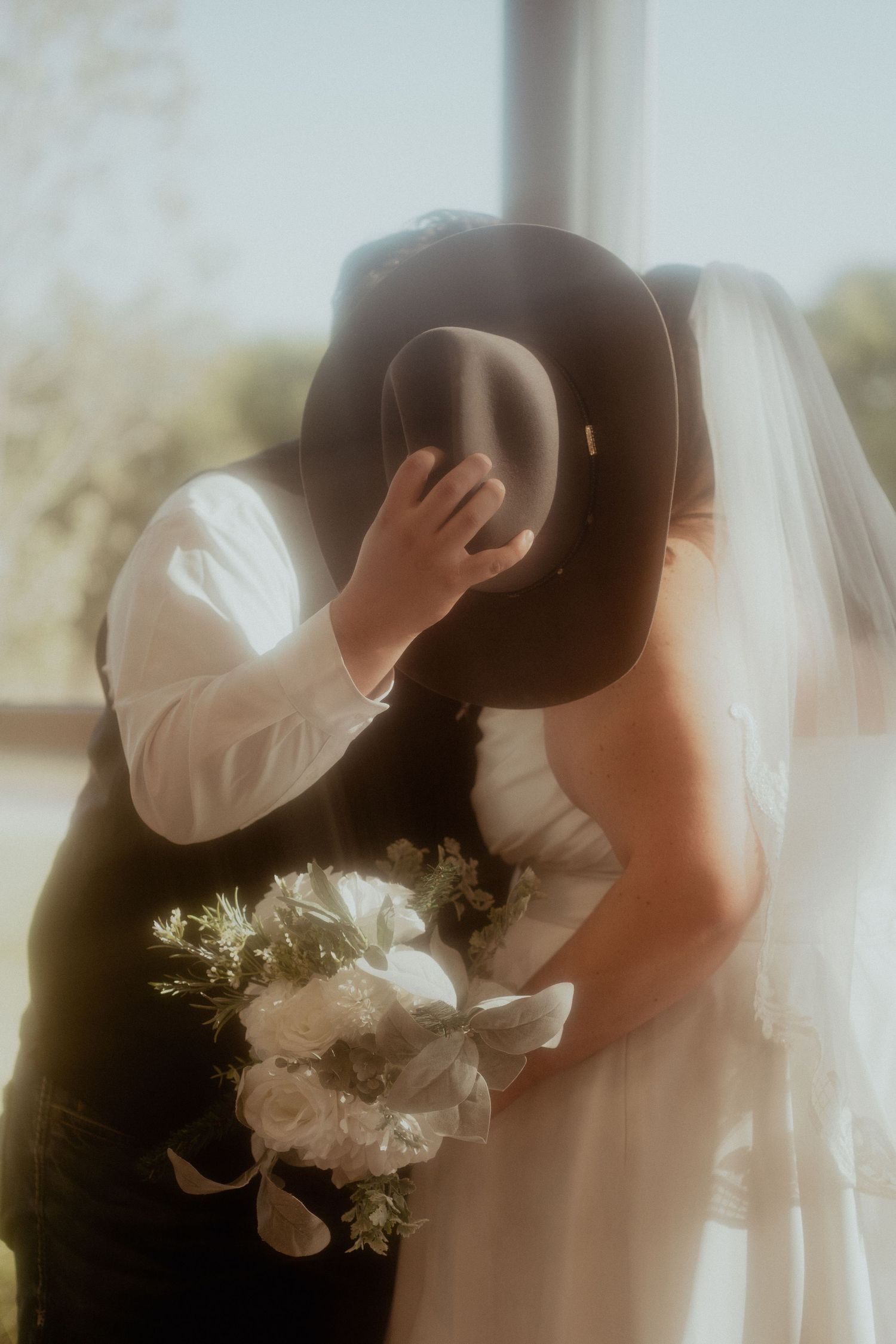 Intimate wedding couple silhouettes in soft focus with white floral bouquet details.