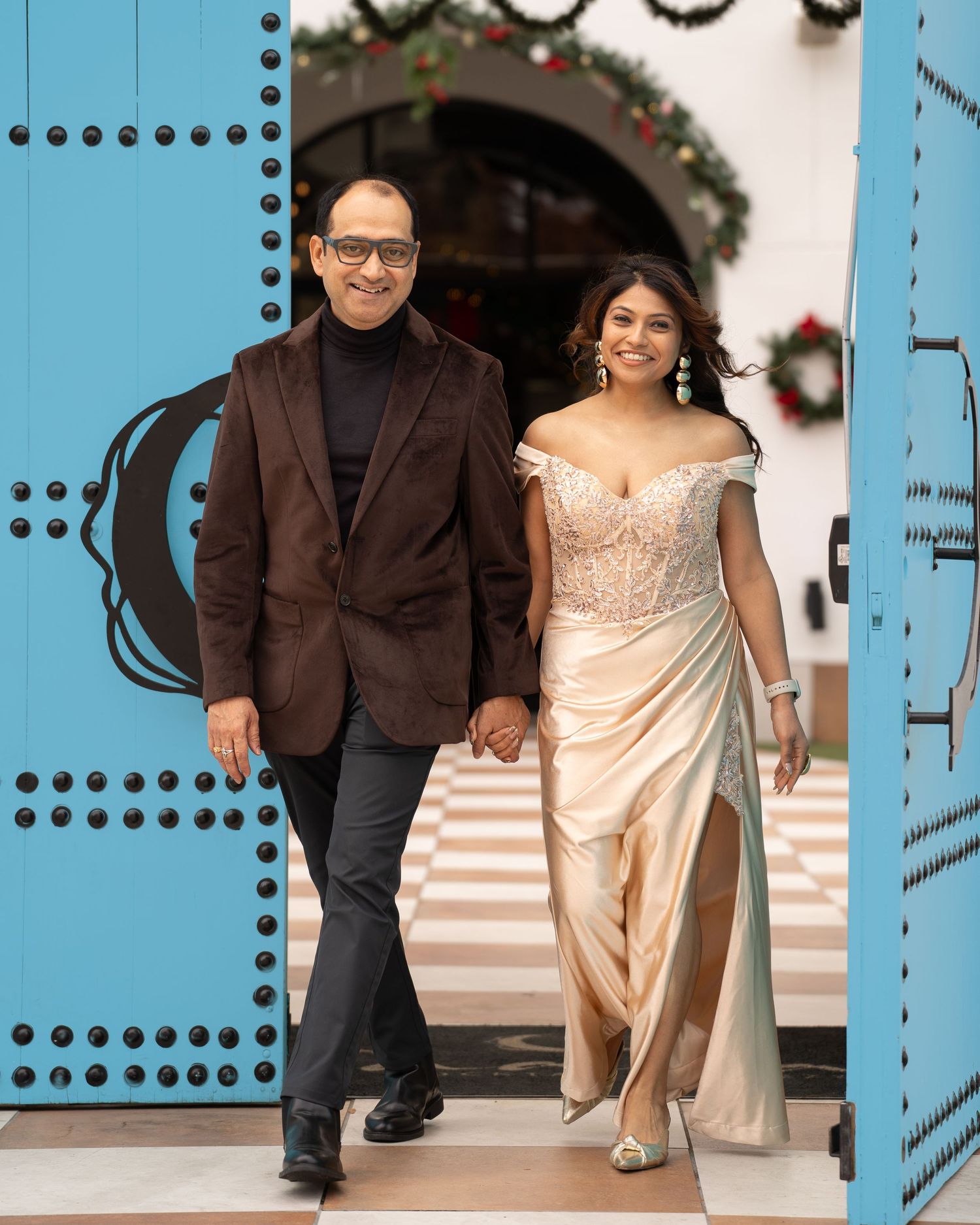 Couple walks through blue doorway wearing formal attire at decorated venue.
