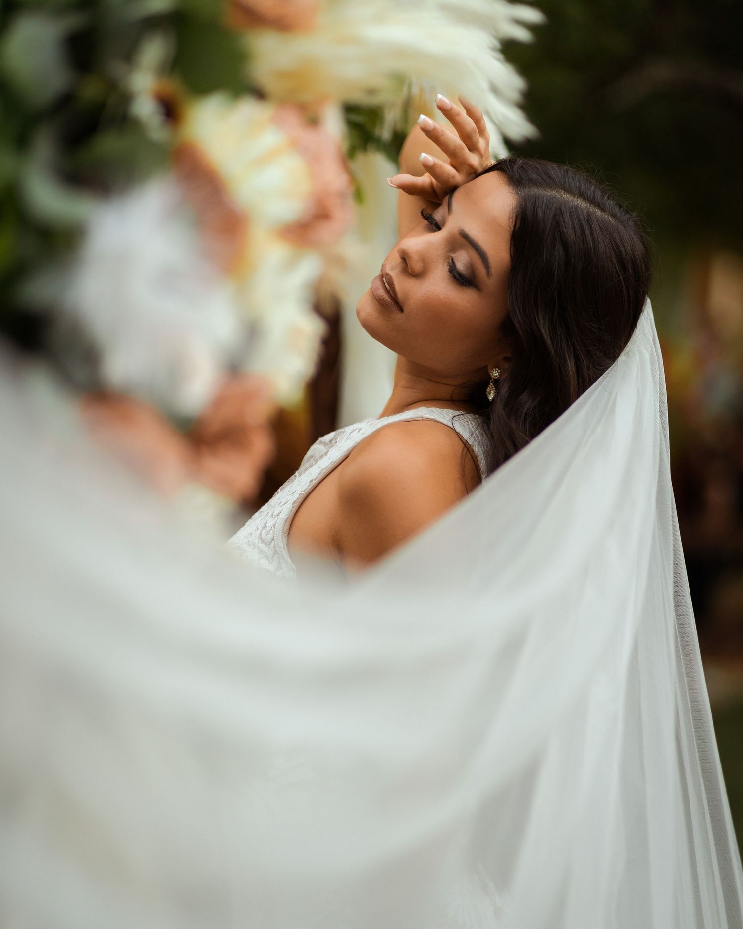 Elegant bride in flowing white veil poses against sunset backdrop during outdoor wedding photoshoot.