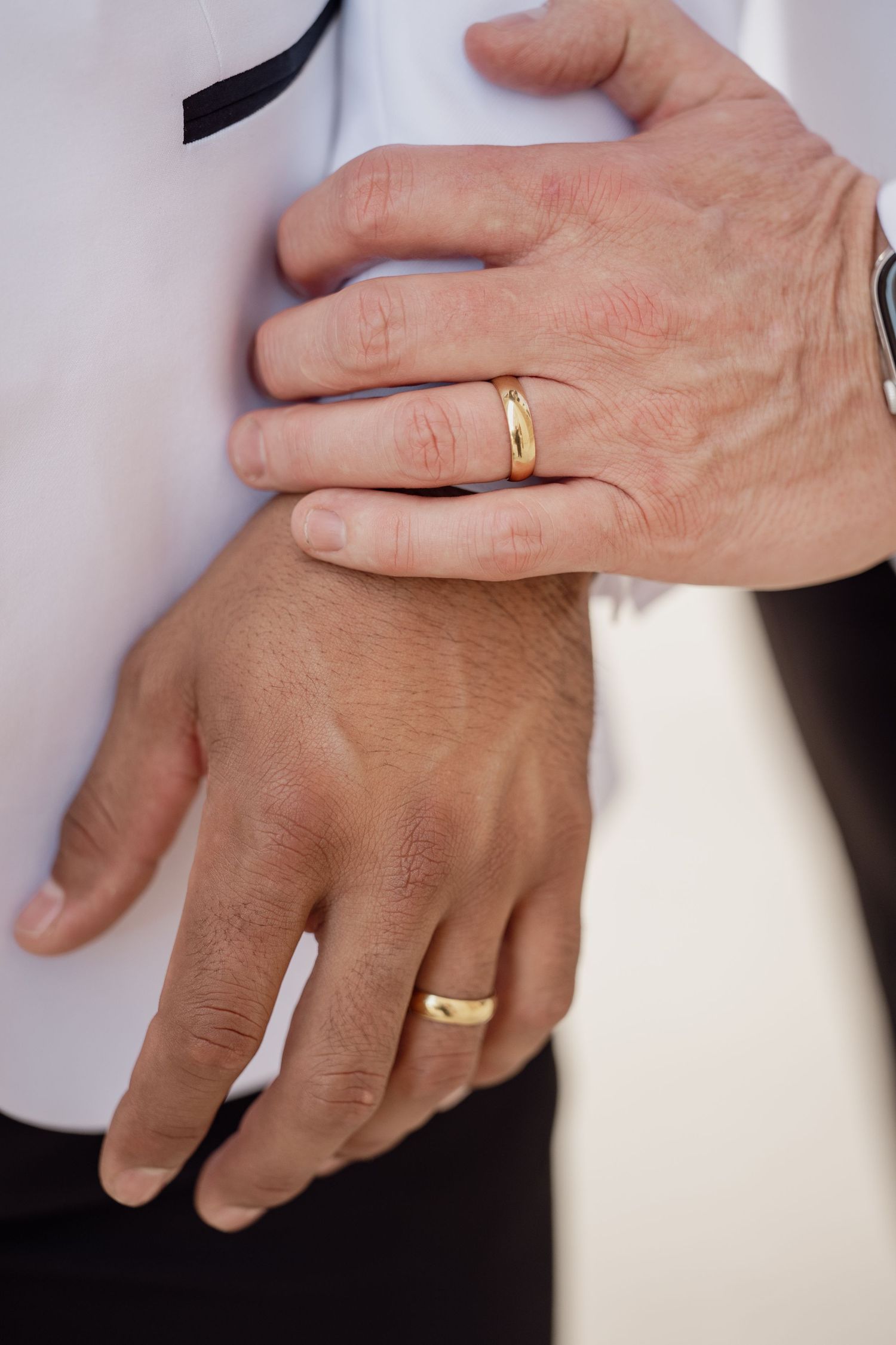 Two men wearing gold wedding bands hold hands, symbolizing love and commitment in a same-sex marriage ceremony.