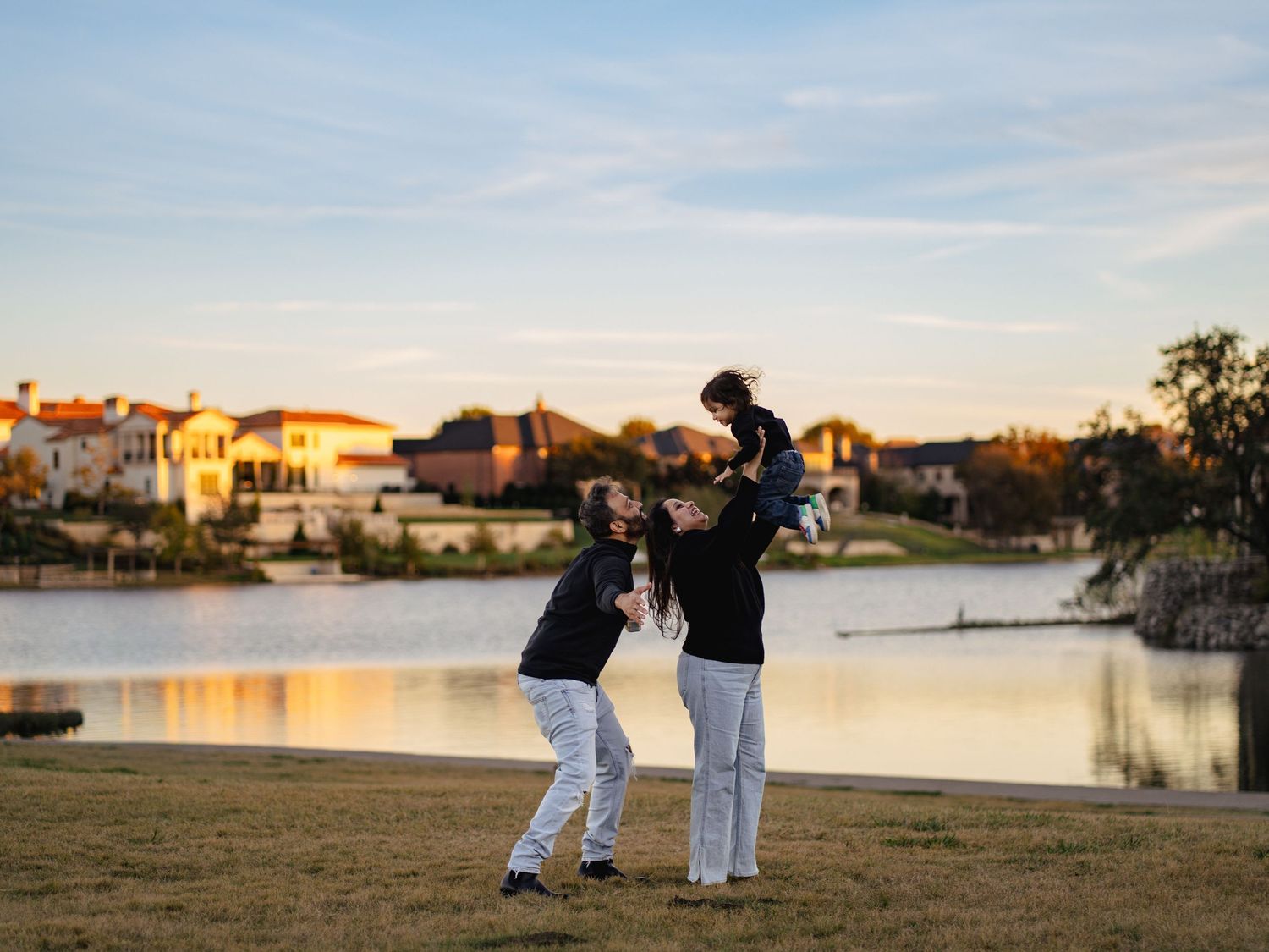 Couple walking along a waterfront path during sunset with city views in the background.