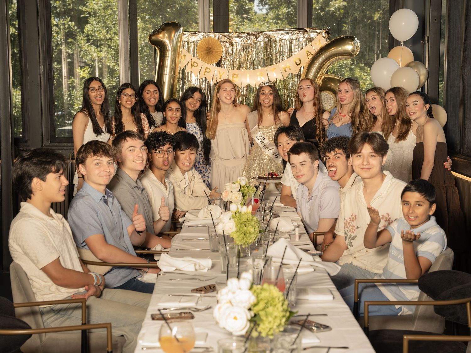Group of teens celebrating a 16th birthday party at an elegant dinner table with gold balloons and floral centerpieces.