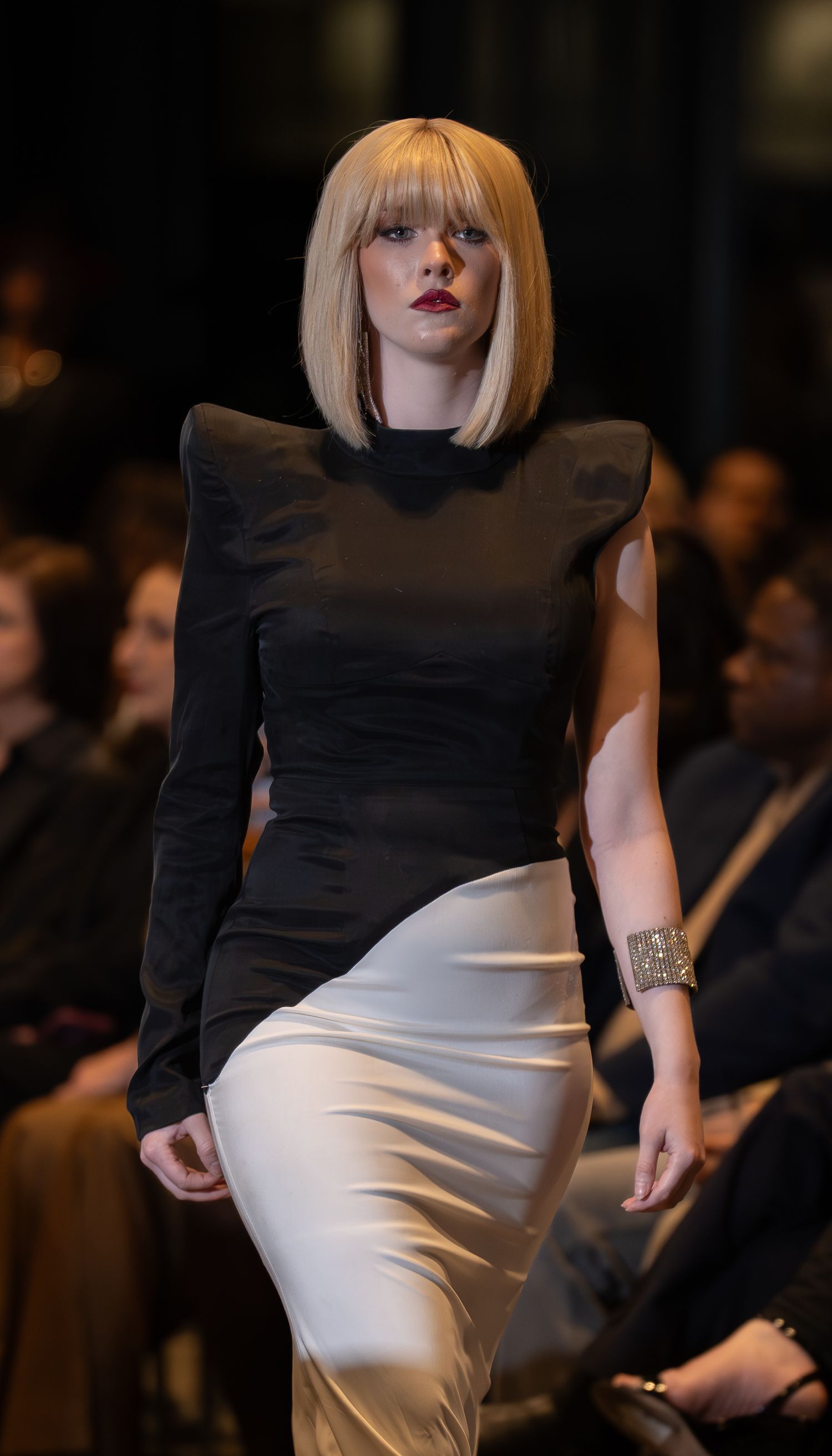 Fashion model walks runway wearing black and white color block dress during fashion show event.
