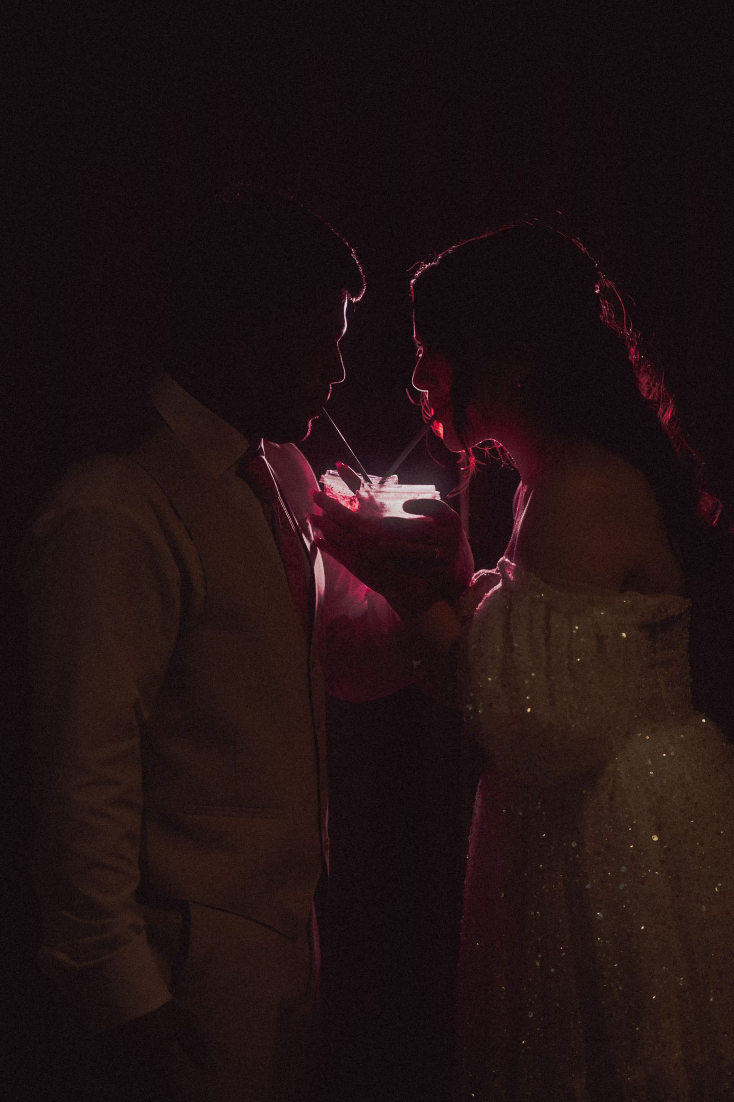 Silhouetted couple dancing in dramatic red lighting at wedding reception.