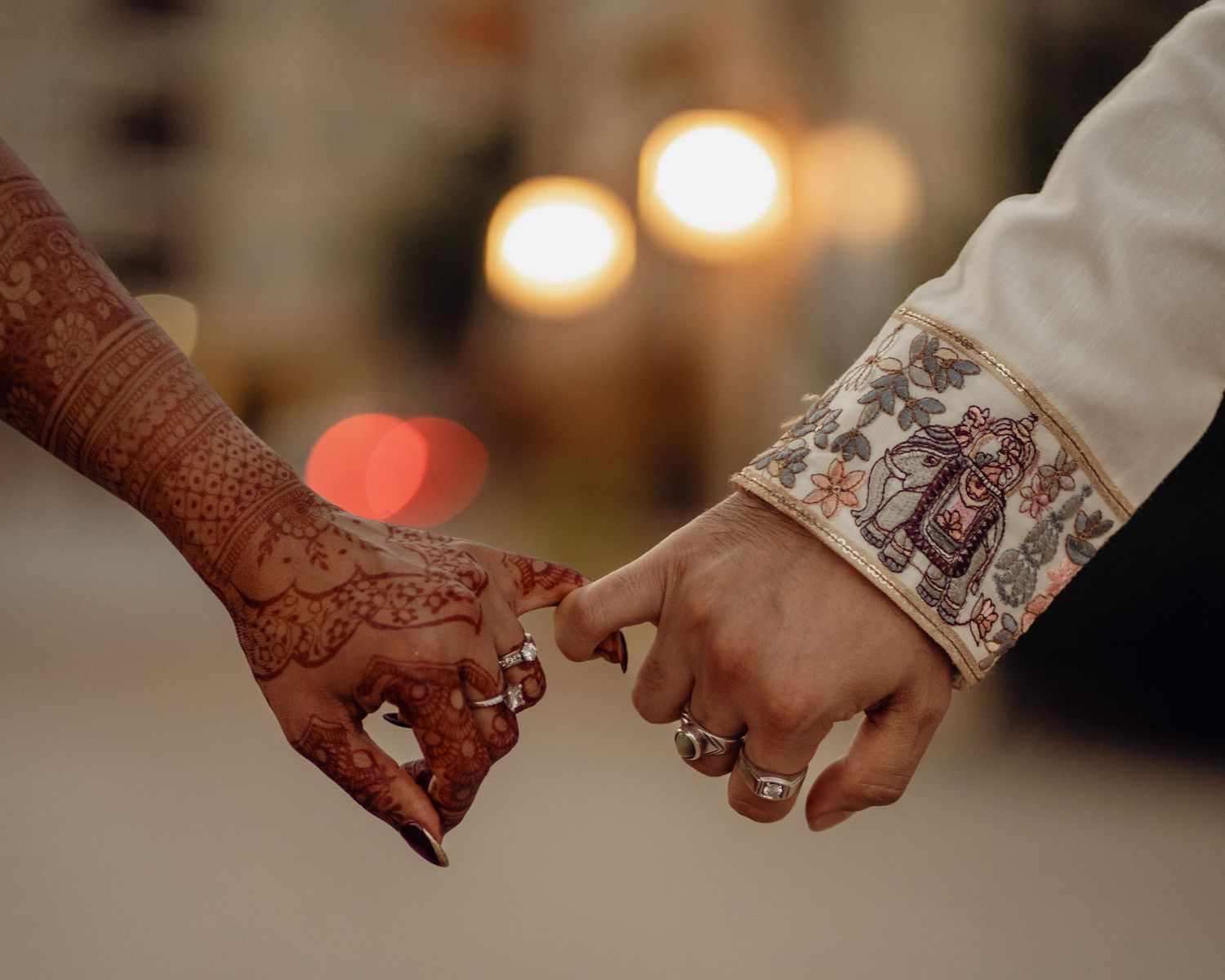 Close-up of decorated hands holding each other with warm lighting in the background.