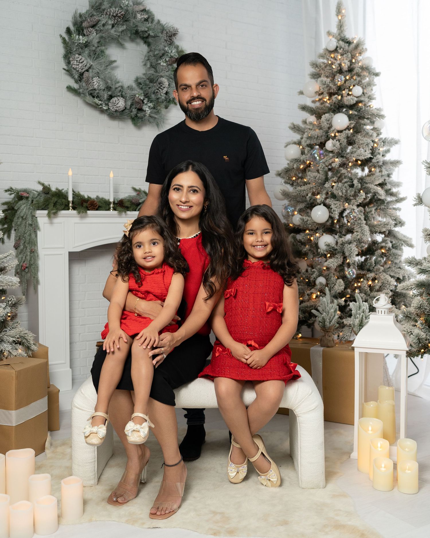 Family wearing red outfits poses together on white floor with Christmas decorations and candles.
