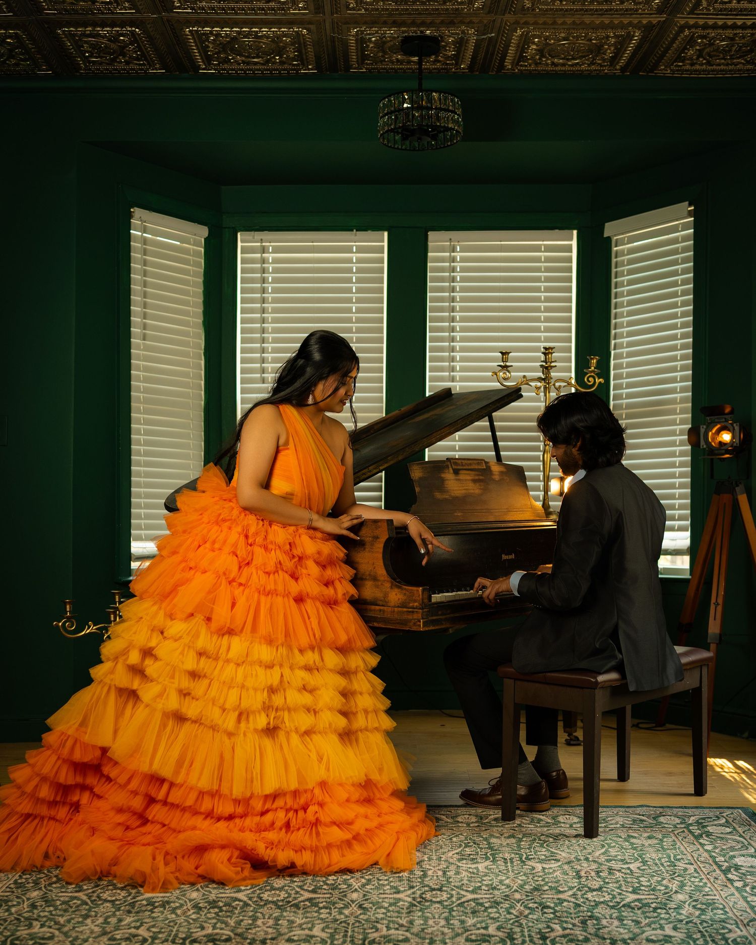 Person in vibrant orange gown posing near piano in dimly lit room.