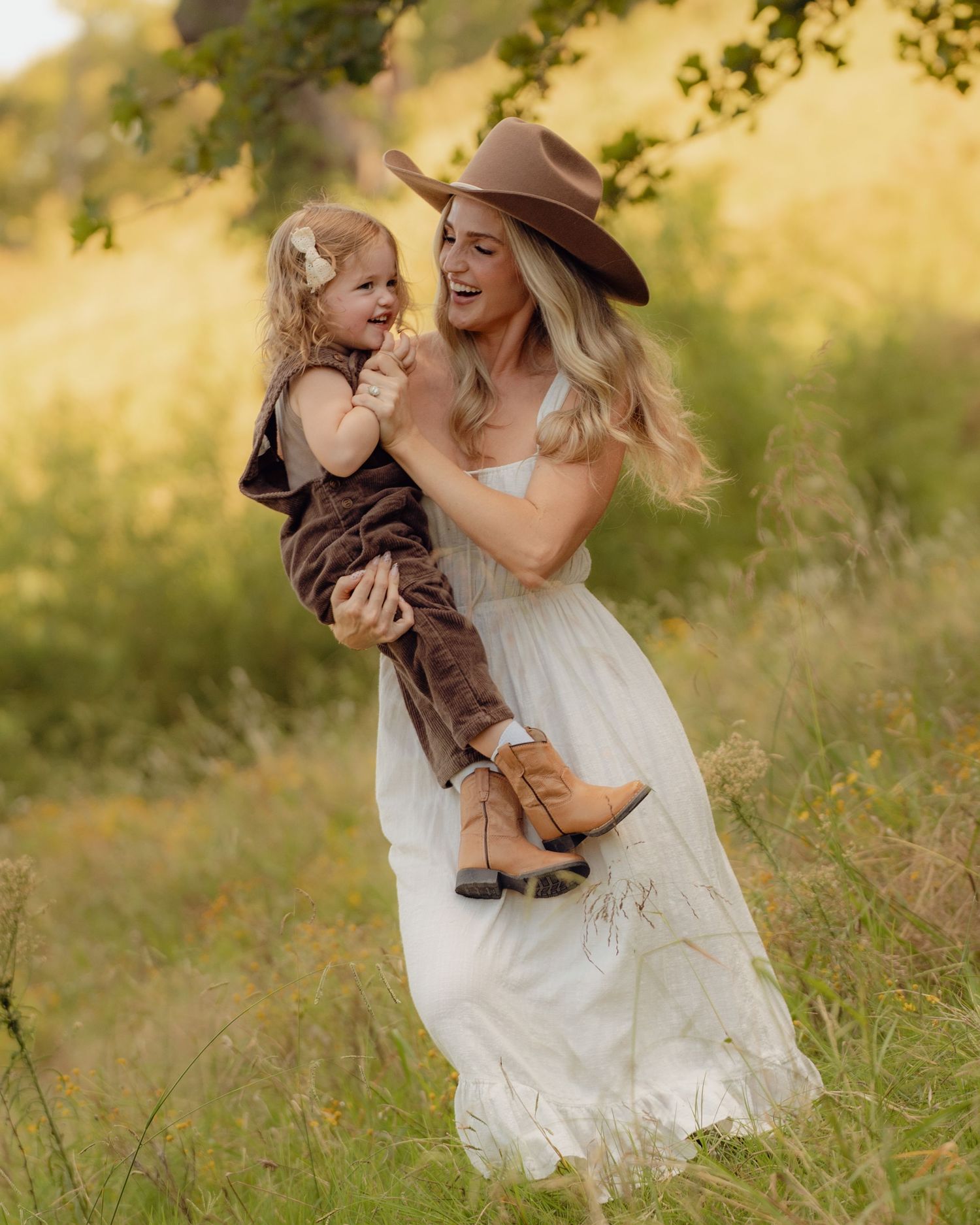 Family enjoying playful moments together in a sunny meadow wearing casual country attire.