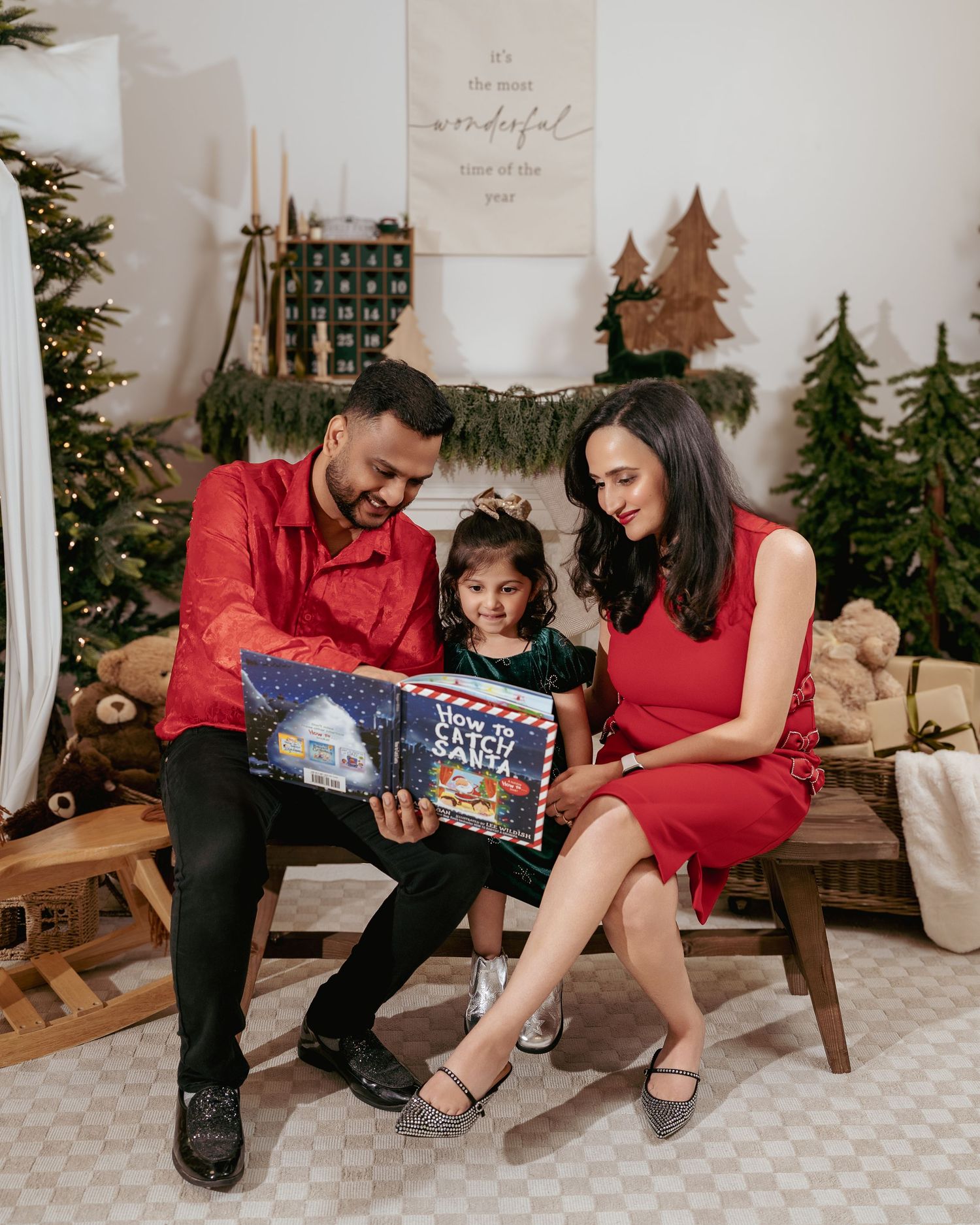 Family of three reading a Christmas book together in a festive holiday setting with Christmas trees and decorations.