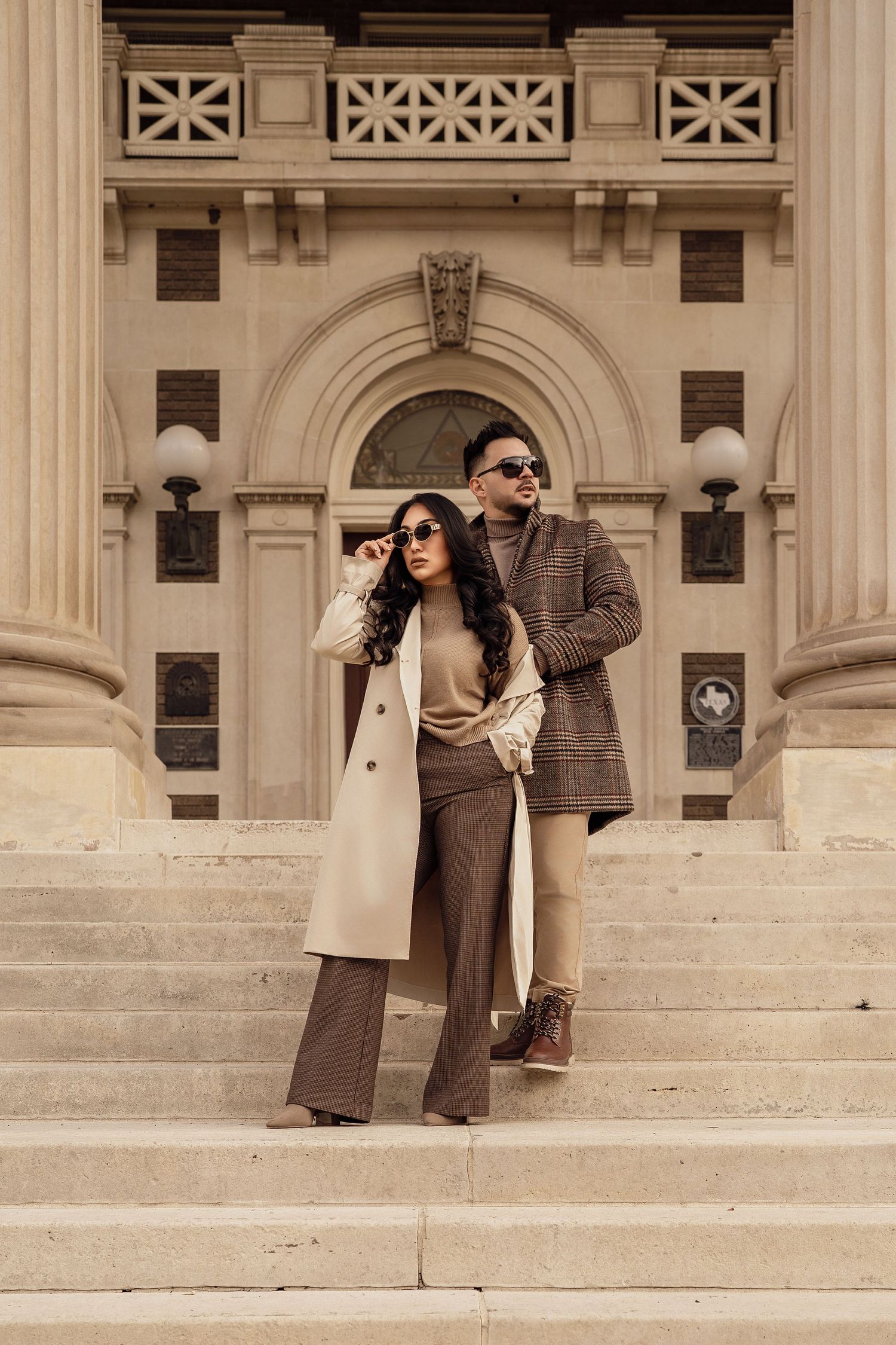 Stylish couple posing on grand stone steps of historic building.