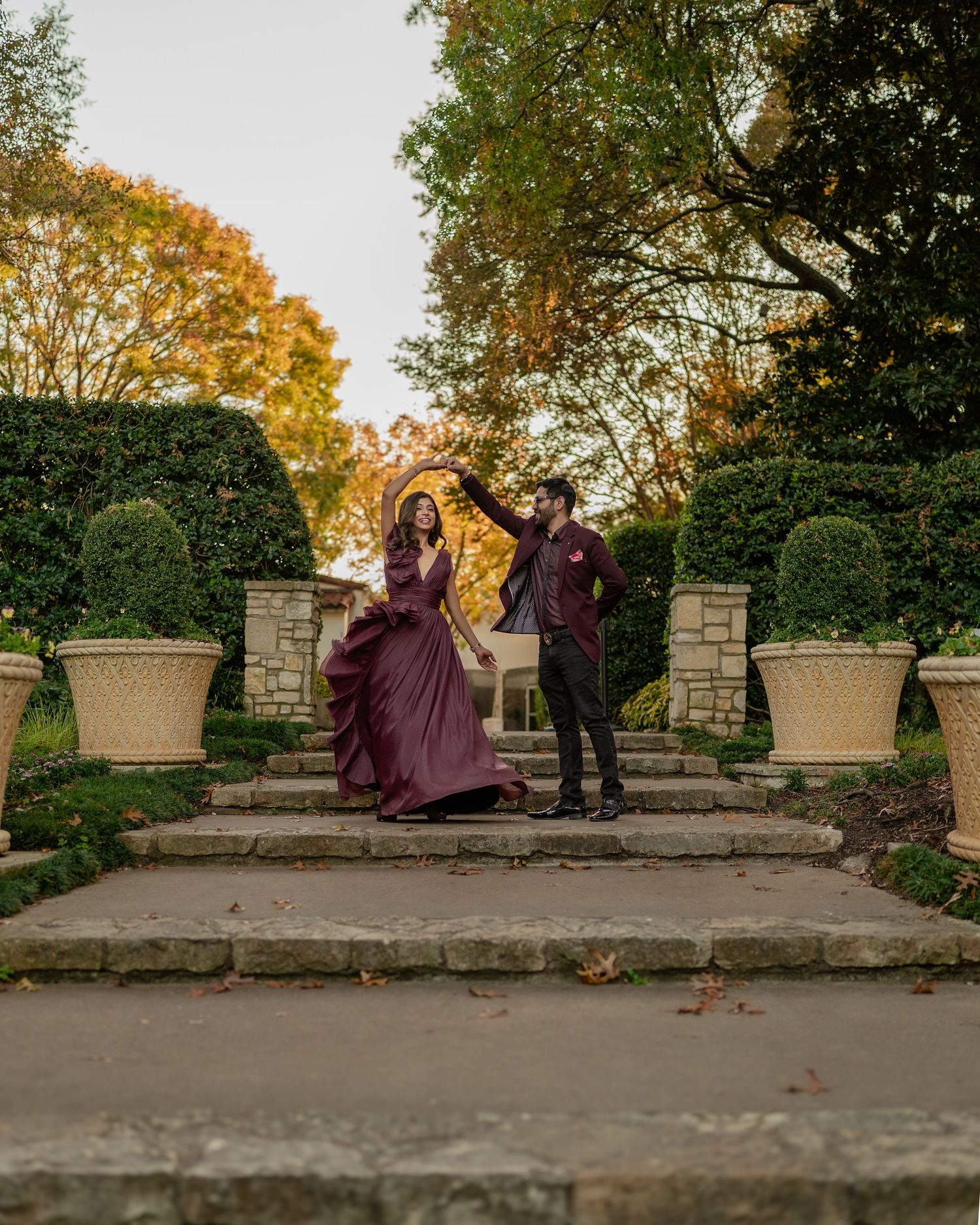 Couple dancing playfully on stone steps surrounded by autumn foliage in a garden setting.