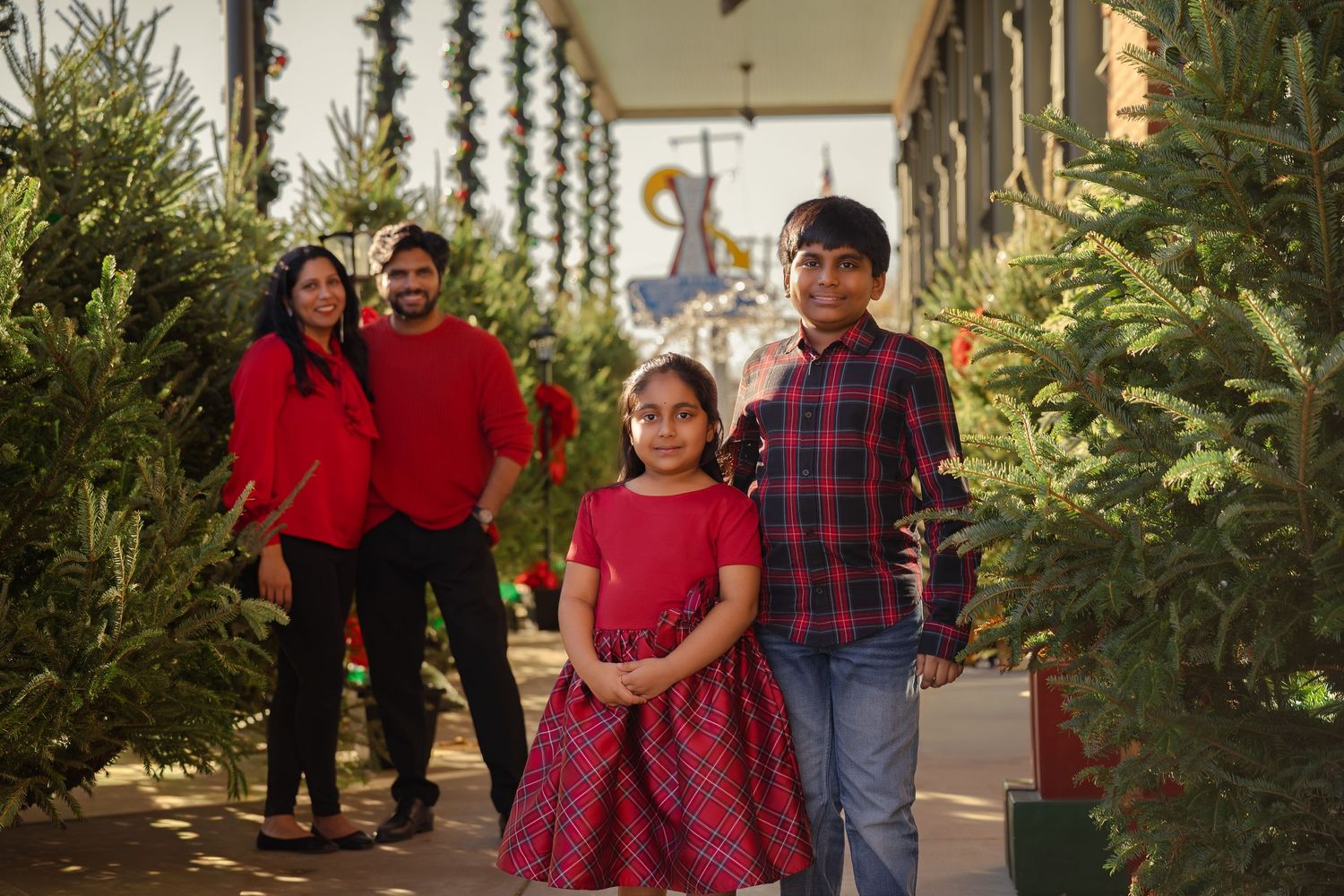 Family of four in red outfits posing among Christmas trees at a festive holiday tree lot.