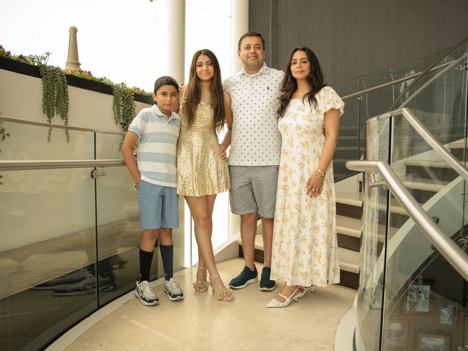Family of four posing together on a modern staircase, dressed in smart casual outfits for a special occasion.