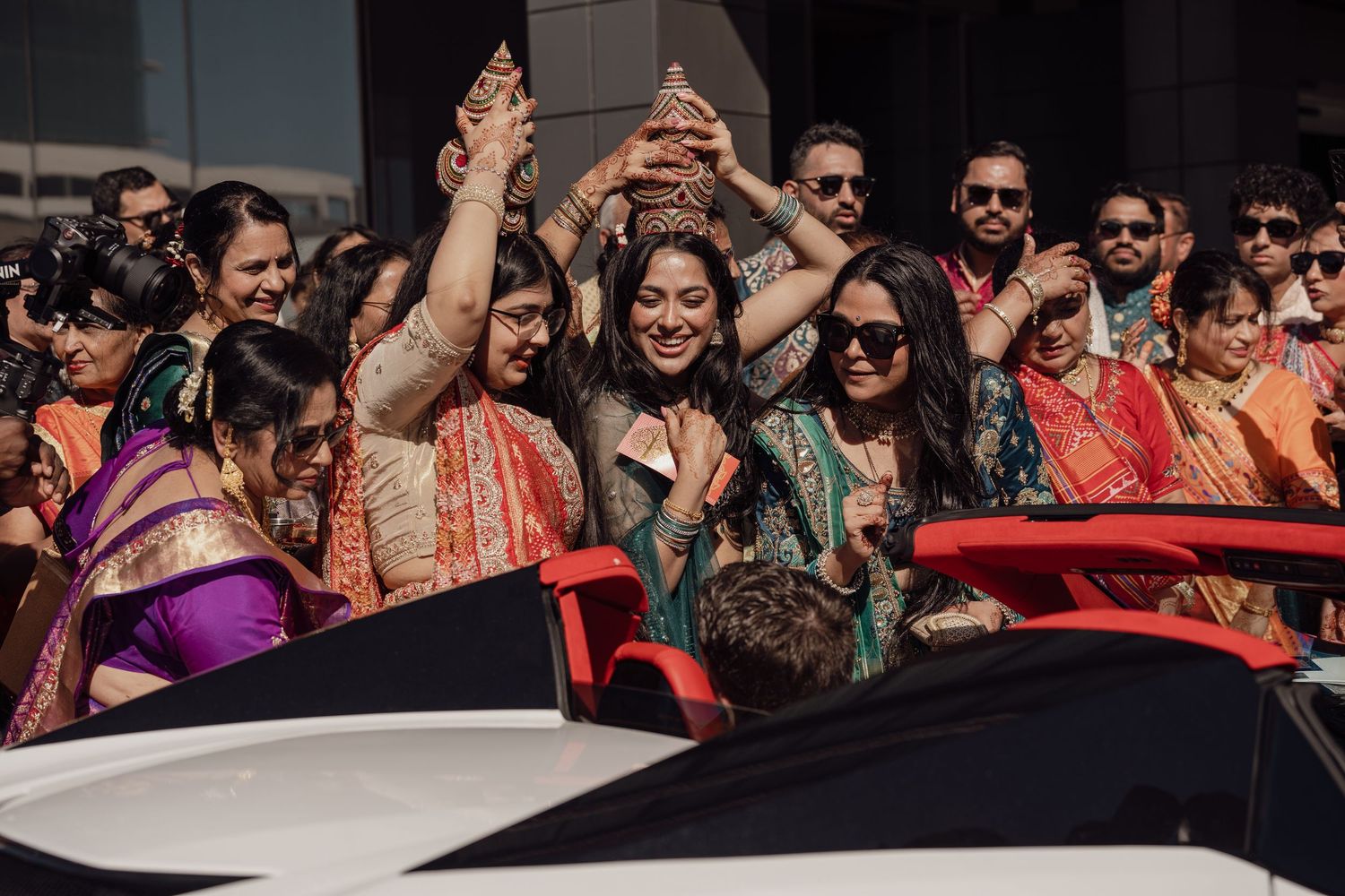 Joyful Indian wedding celebration with guests in colorful traditional attire raising hands outdoors.