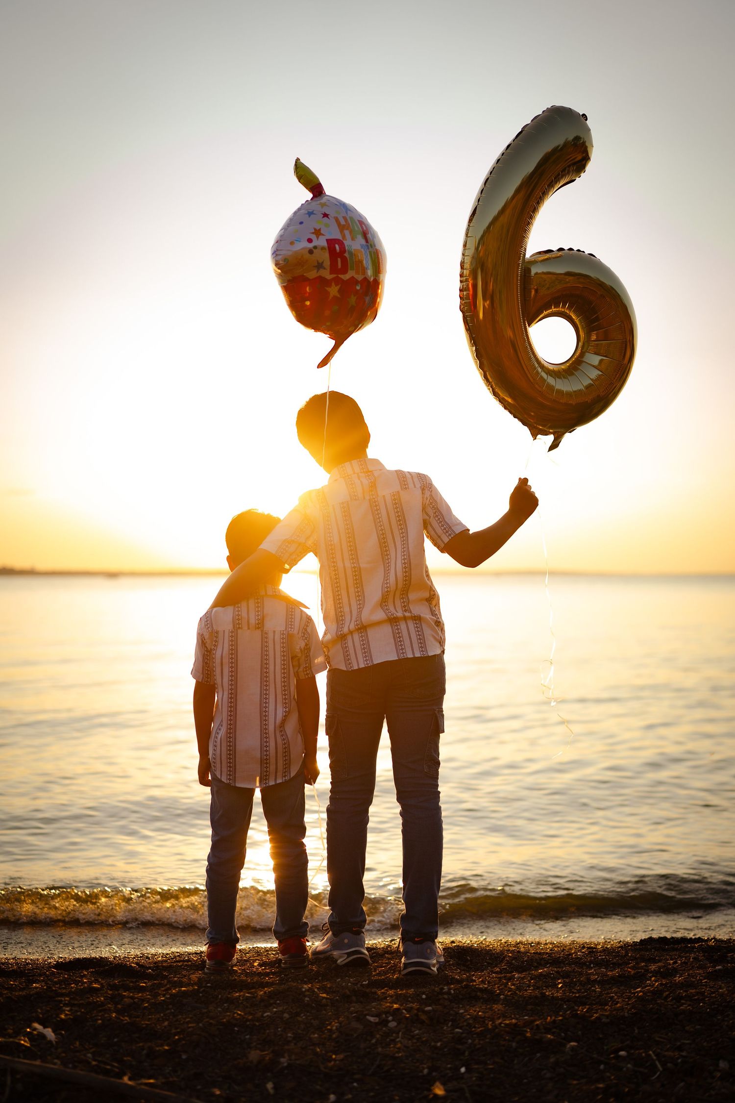 Silhouettes of children holding number balloons on beach at sunset.