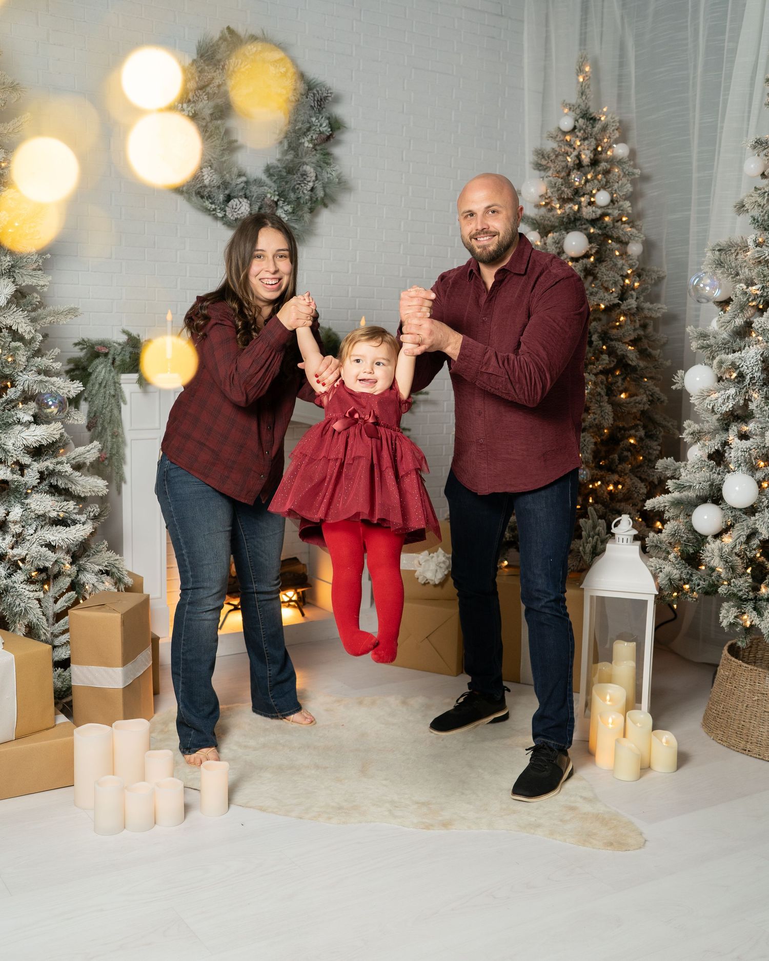Candid family moments captured in burgundy outfits against winter holiday backdrop with snow-covered trees.