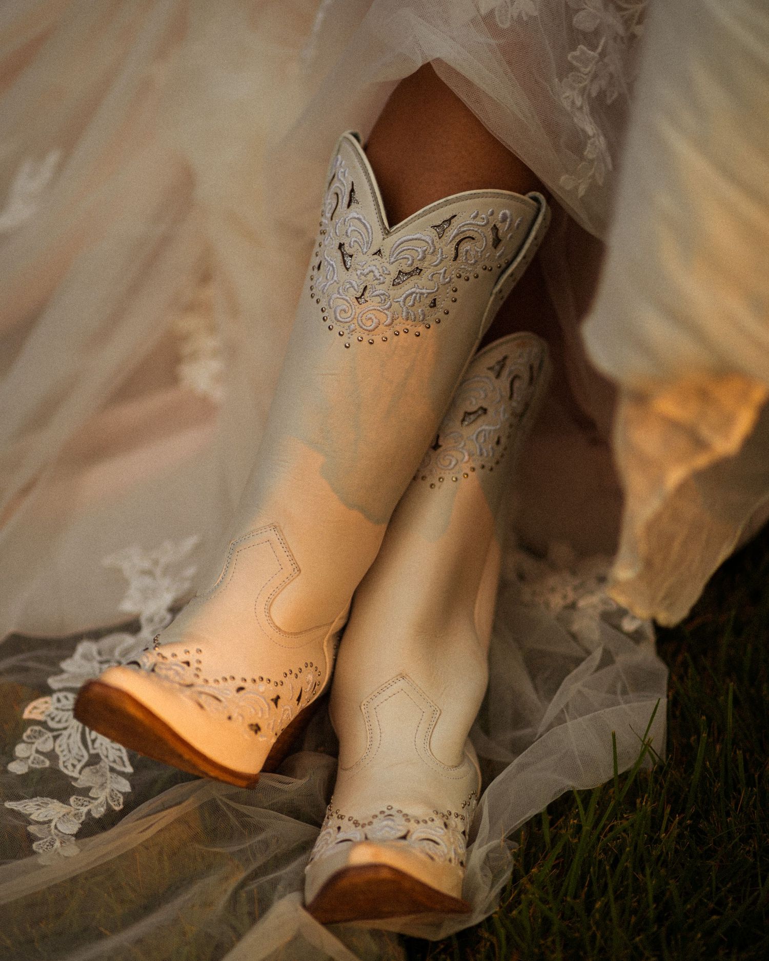 Close-up detail of ornate bridal shoes with lace and crystal embellishments on grass.