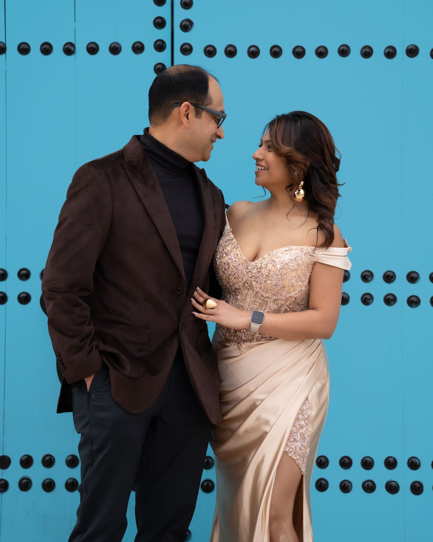 Stylish couple poses against bright blue wall in formal evening wear.