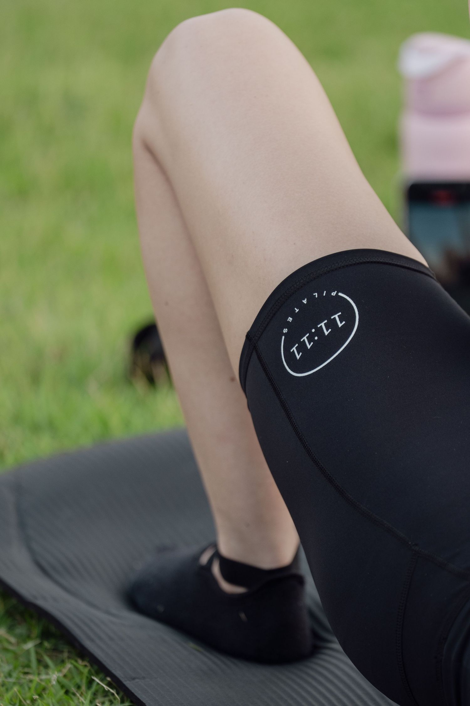 Woman wearing black ELITE branded workout shorts on a yoga mat outdoors on green grass.